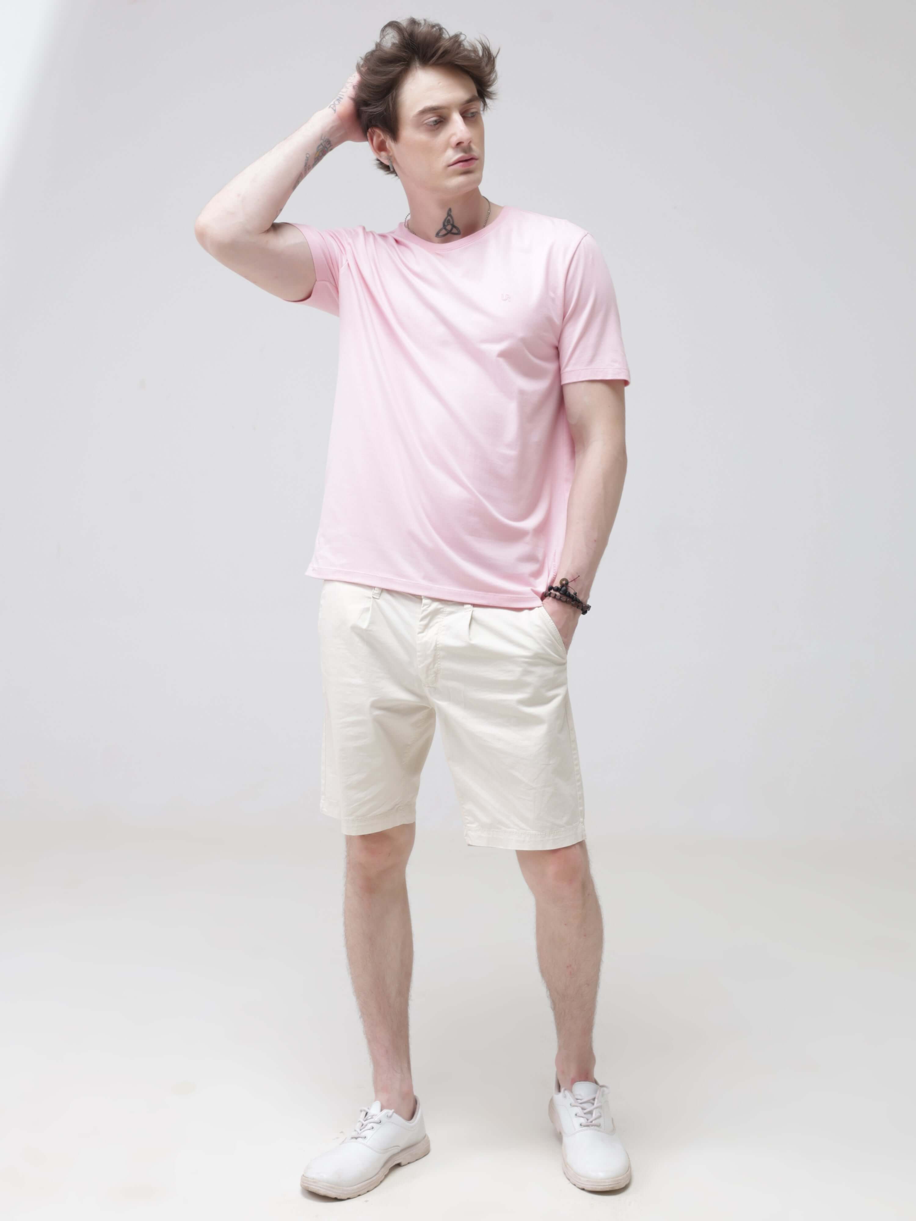 Man wearing a pink stain-proof and odor-resistant Turms T-shirt with tailored fit and round neck, paired with white shorts and white shoes.