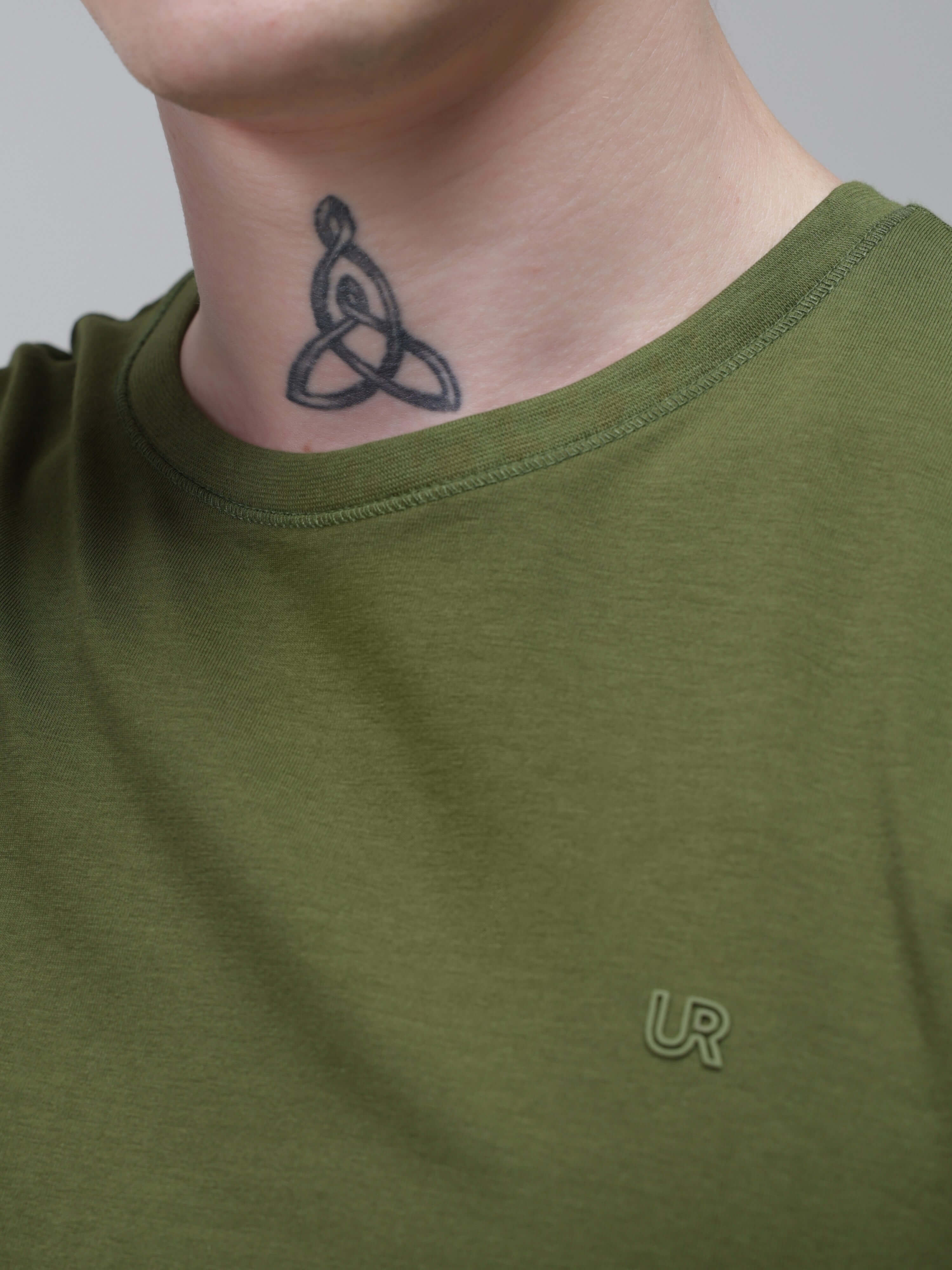 Man wearing green round-neck Turms T-shirt, featuring stain-proof and water-resistant properties, with visible tattoo on neck.