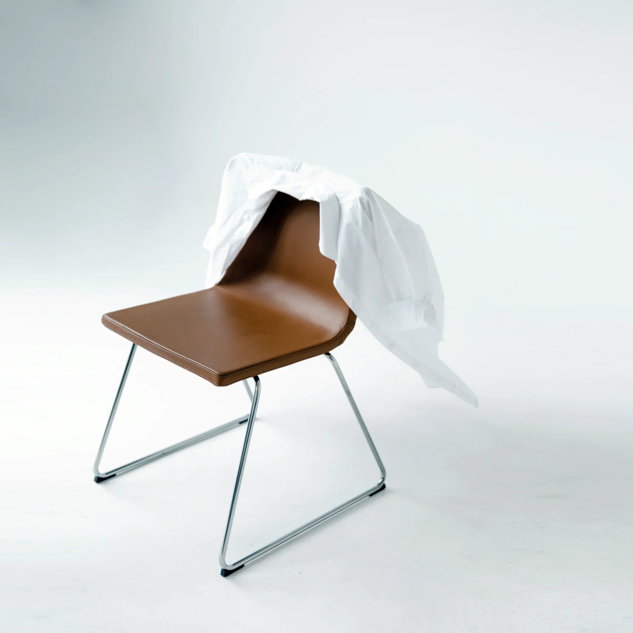 Minimalist brown chair with a white tablecloth draped over it, set against a light background.