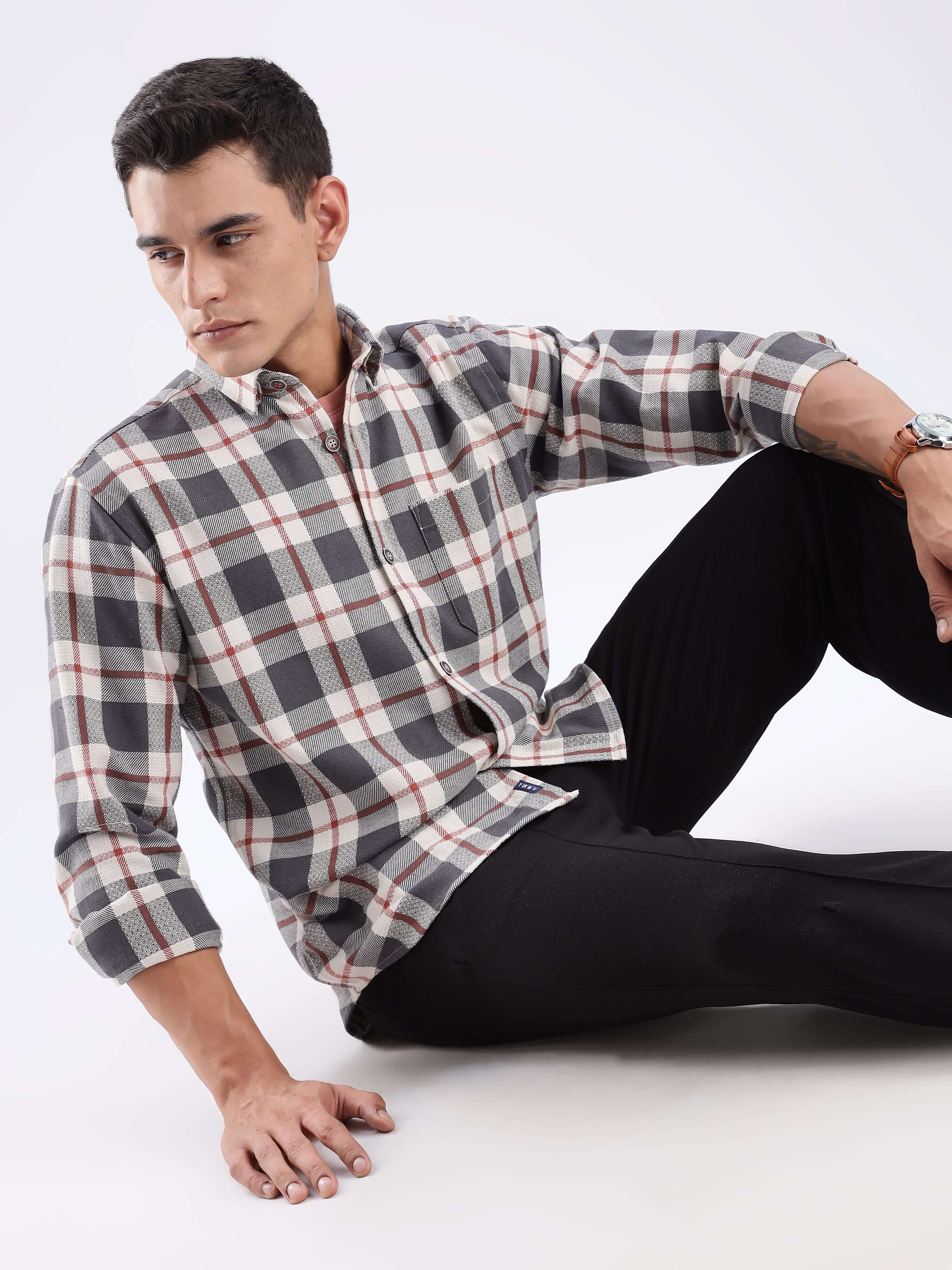 Man seated wearing a grey checked shirt made from recycled cotton, showcasing sustainable style and comfort.