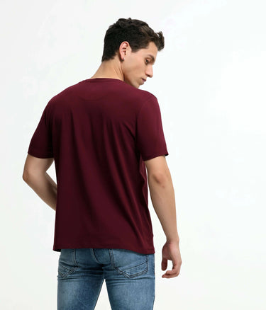 Man wearing cranberry round-neck Turms T-shirt, tailored fit, stain-proof and odor-resistant, paired with blue jeans.