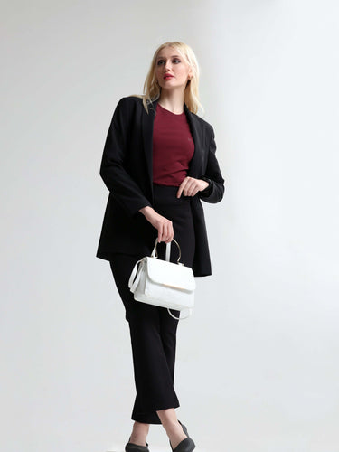 Woman in a black blazer and pants with a red round-neck T-shirt holding a white handbag.