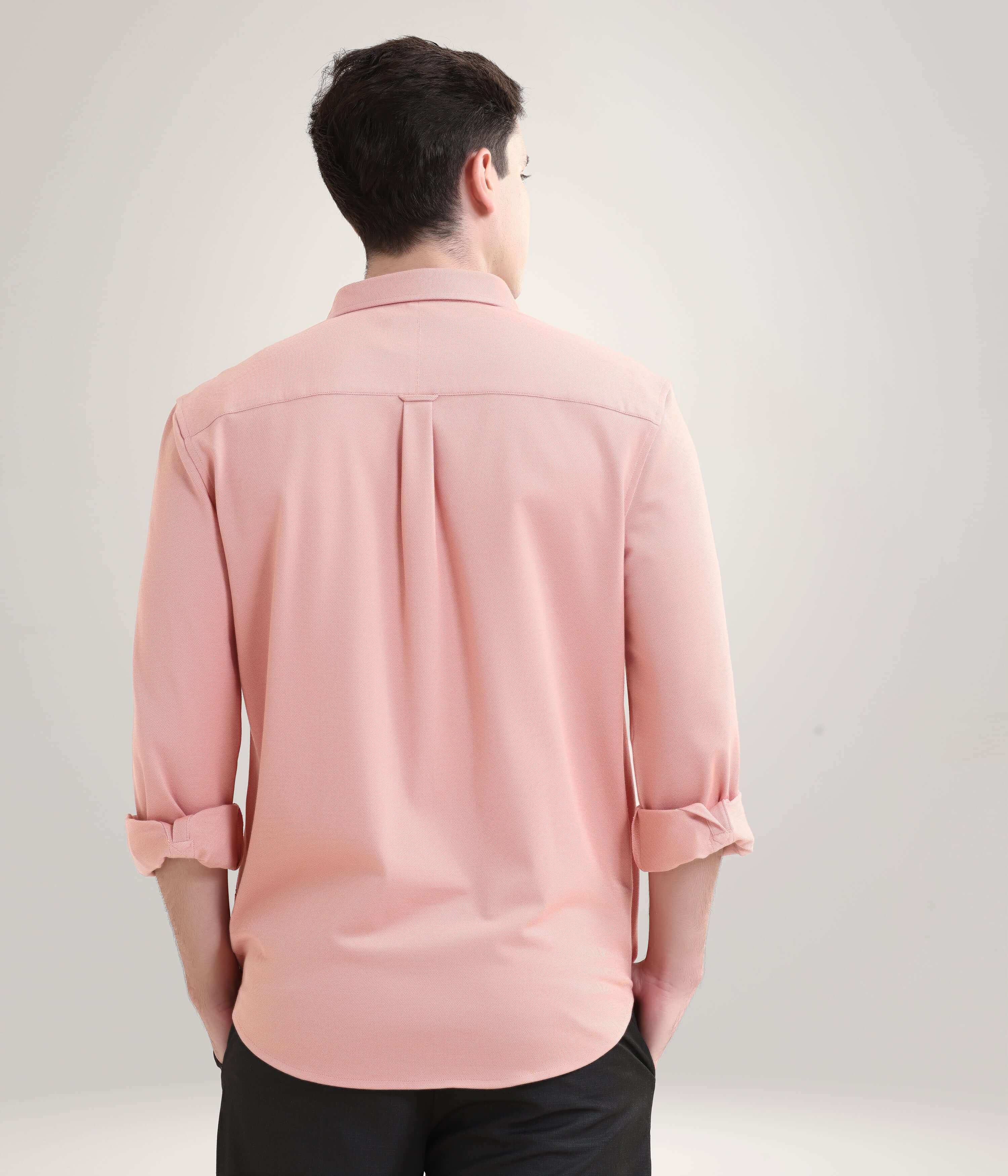 Man wearing pink shirt with rolled sleeves, viewed from the back against a light background.