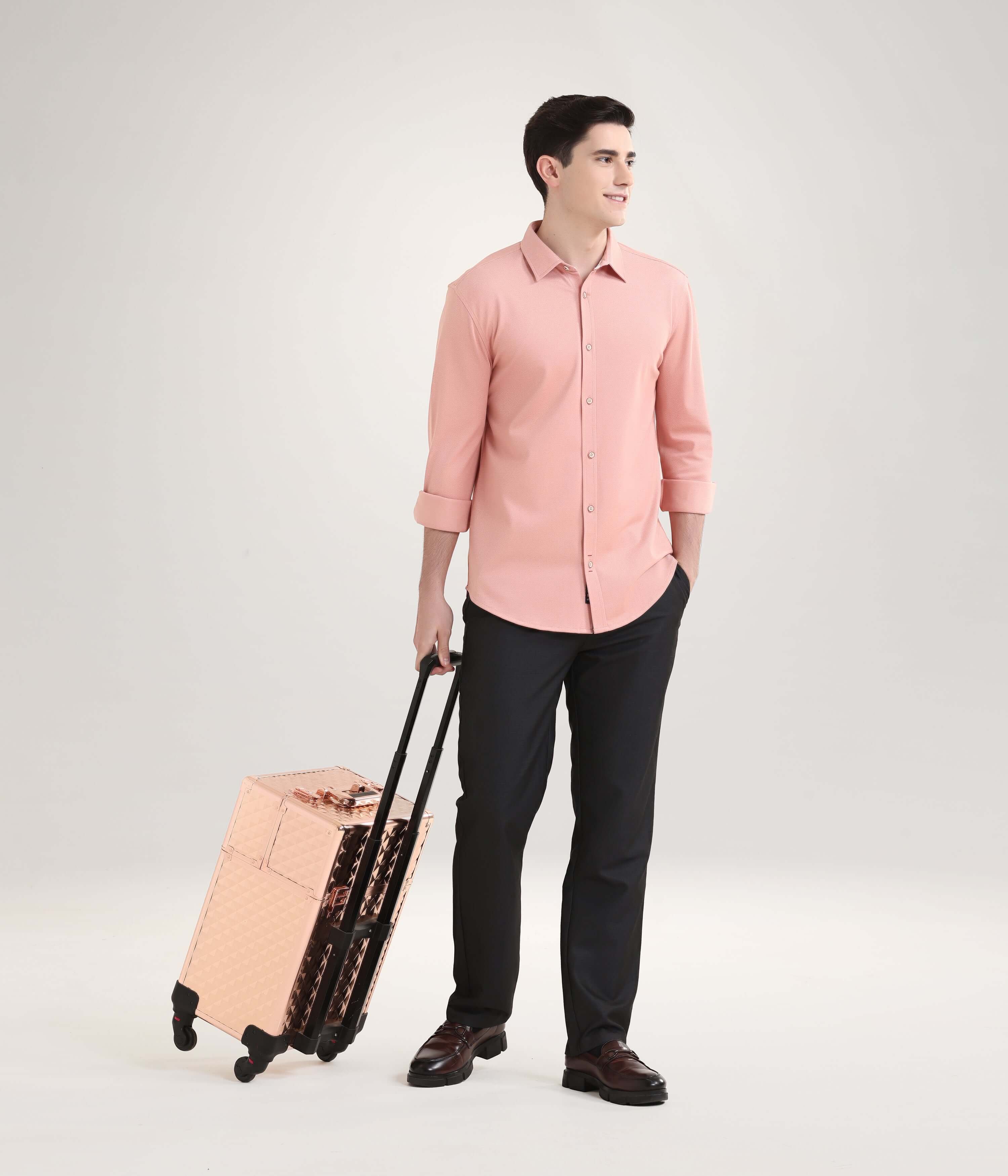 Man wearing a rustic orange knitted shirt standing with a copper suitcase, showcasing premium menswear fashion in a stylish setting.