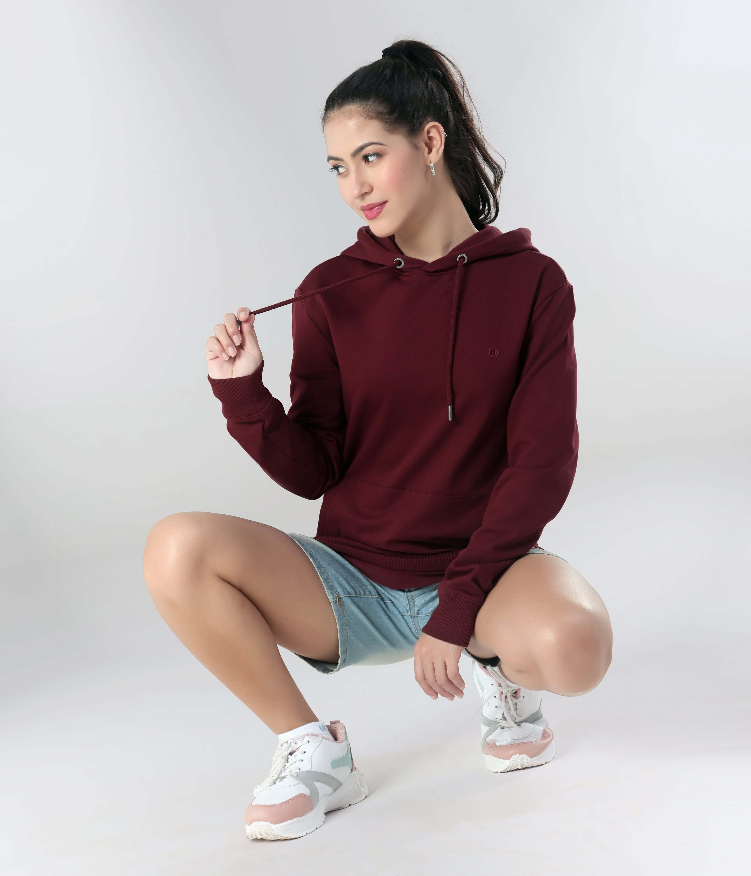 Stylish woman in a maroon hooded sweatshirt, perfect for travel wear, showcasing comfort and sporty elegance.