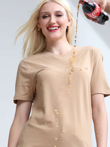 Woman wearing stain-proof Camel round-neck T-shirt smiling while liquid is poured on it.