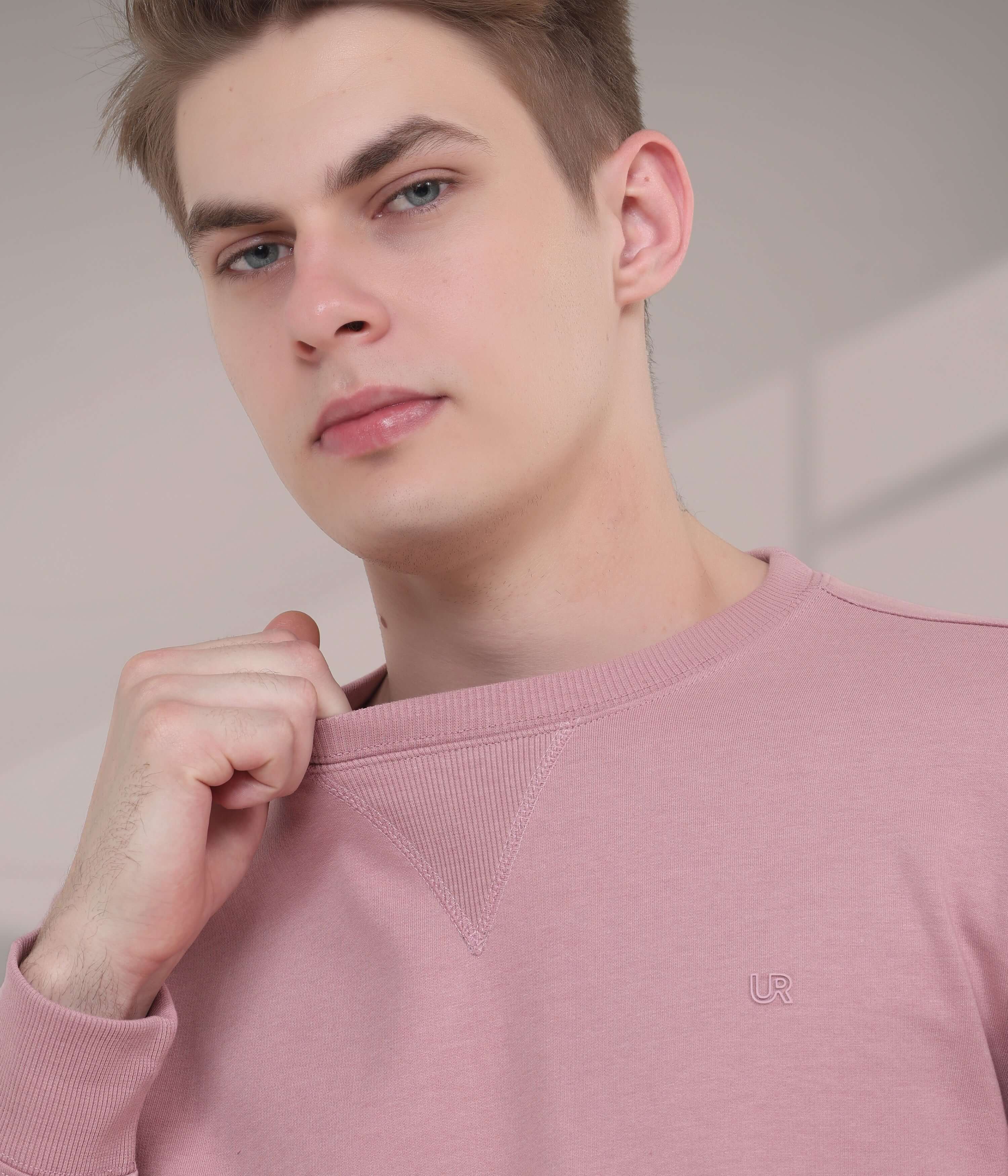 Young man in a pink sweatshirt showcasing a stylish V-notch neckline, embodying comfort and modern menswear trends.