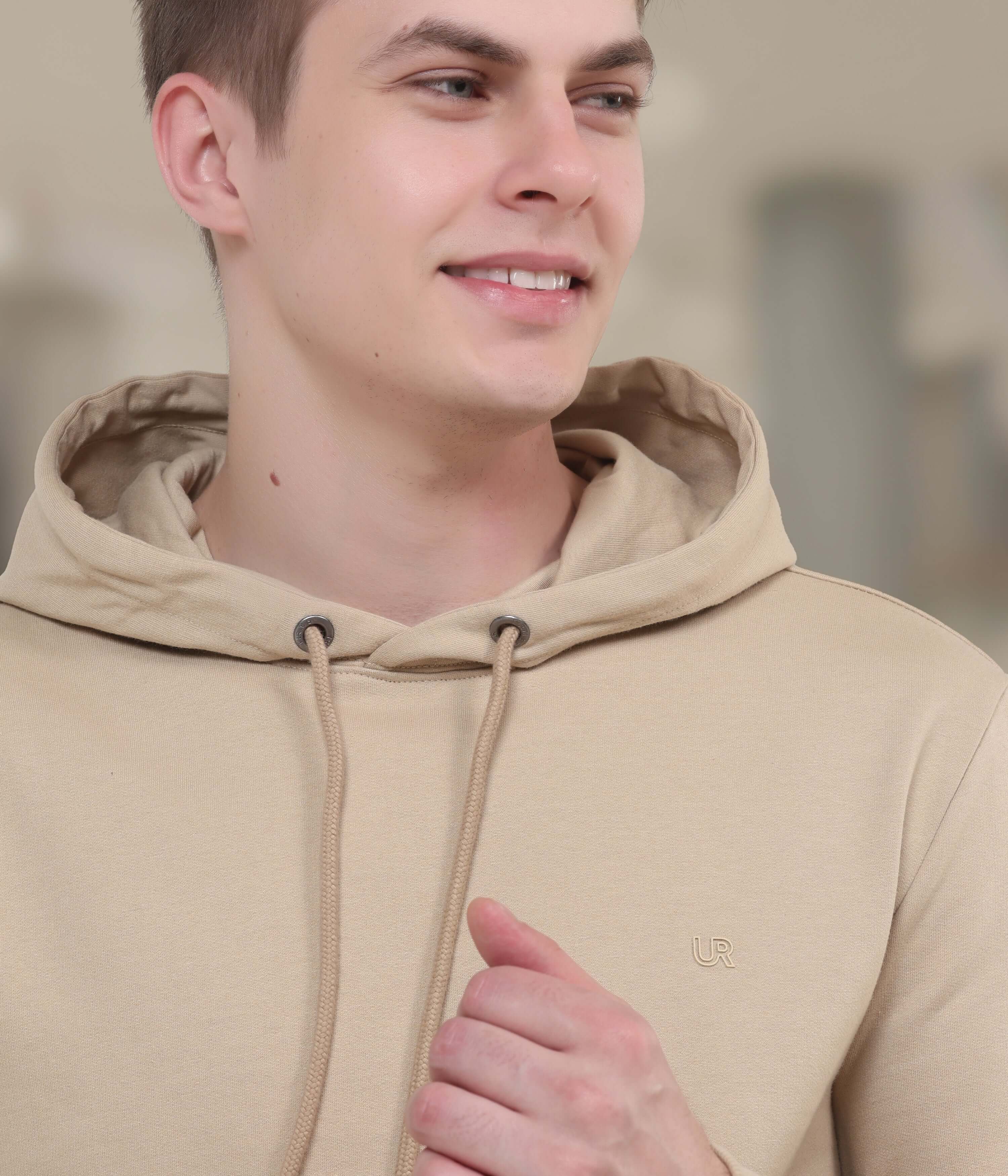 Young man smiling in a beige hooded sweatshirt, showcasing stylish and comfortable design perfect for everyday wear.