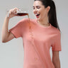 Woman demonstrating stain-proof capability of Sunset Spice Turms T-shirt by pouring liquid on it. Anti-odor, anti-stain cotton fabric.