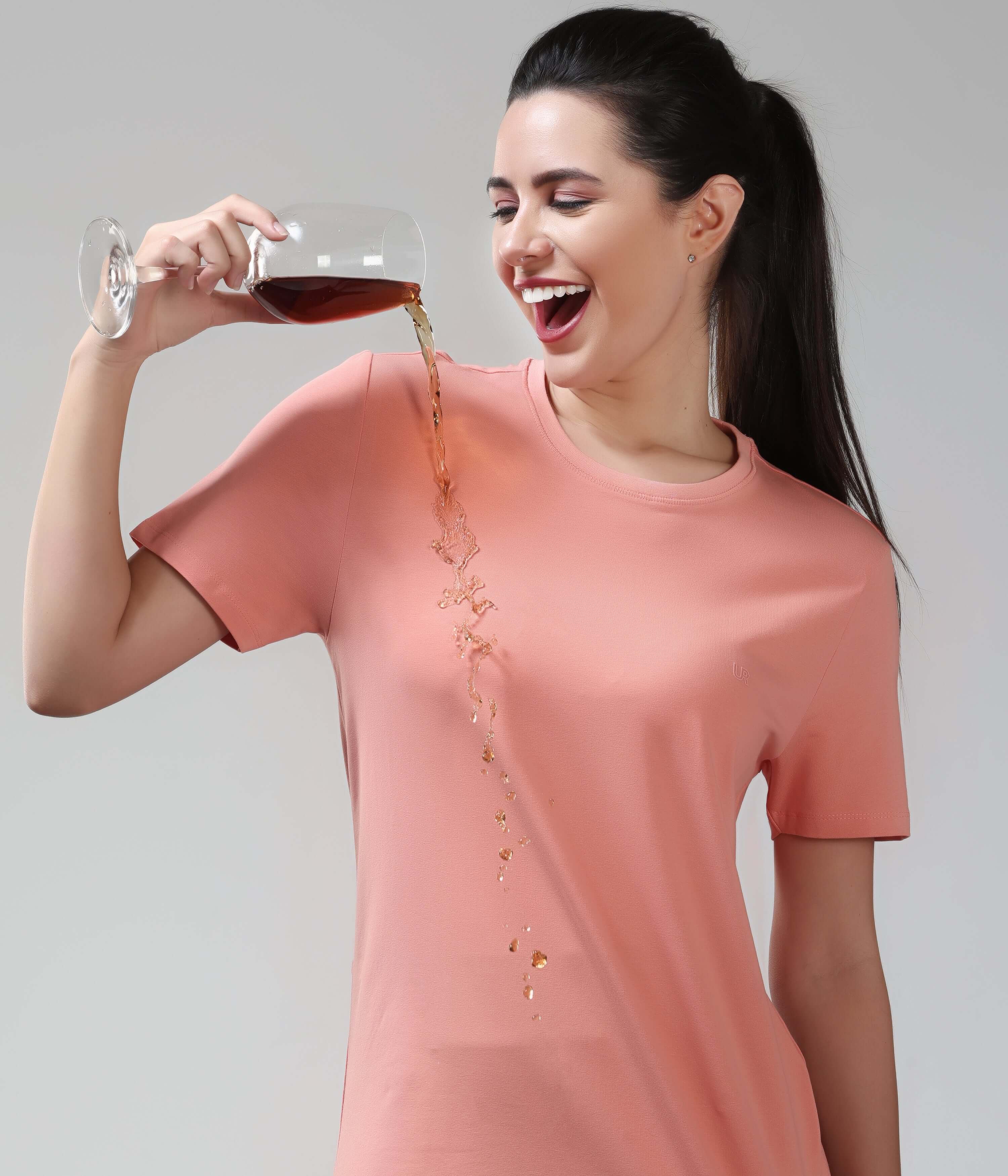 Woman demonstrating stain-proof capability of Sunset Spice Turms T-shirt by pouring liquid on it. Anti-odor, anti-stain cotton fabric.