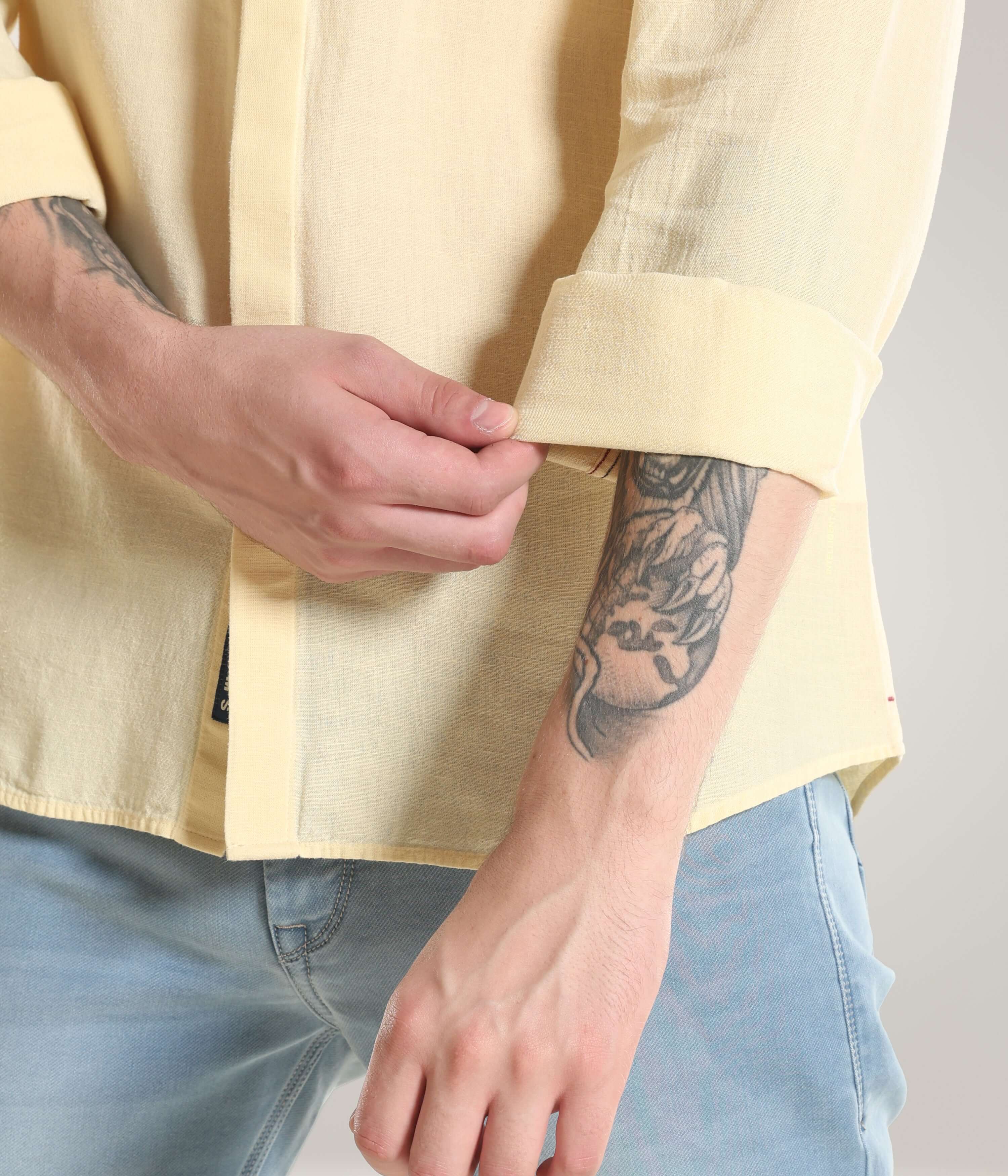 Person wearing a pastel yellow cotton/linen Turms shirt with rolled-up sleeves, showcasing premium stitching and durable fabric.