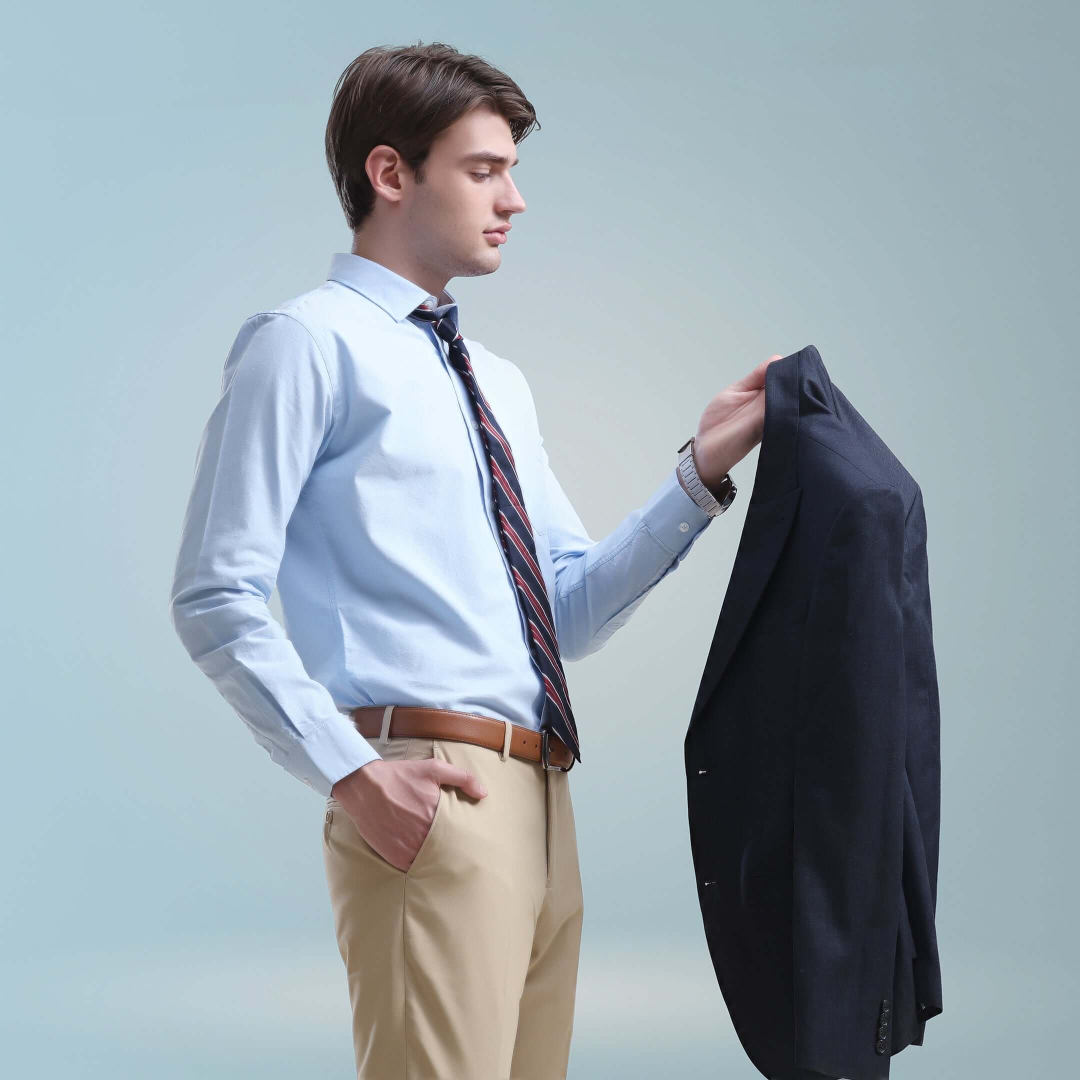 Man wearing a blue Oxford Turms shirt holding a navy blazer, showcasing premium cotton fabric and crisp collar of intelligent apparel