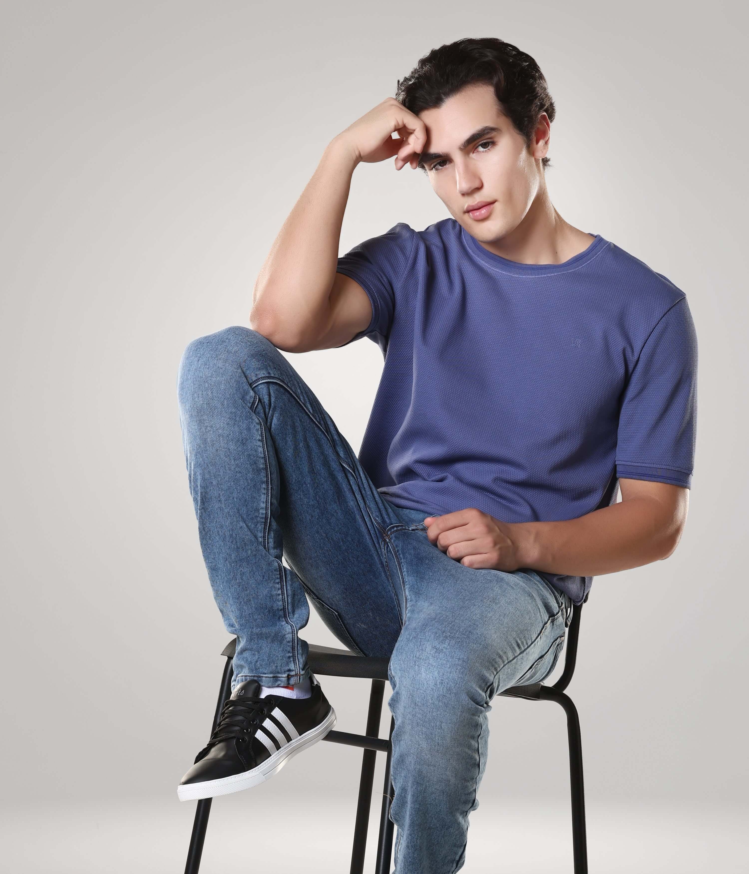 Man wearing a Blooming Orchid Cooltech Cotton Round-Neck Turms T-shirt paired with jeans sitting confidently on a chair.