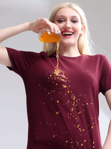 Woman wearing cranberry stain-proof, odor-resistant round-neck Turms T-shirt demonstrating spill resistance with liquid pour.