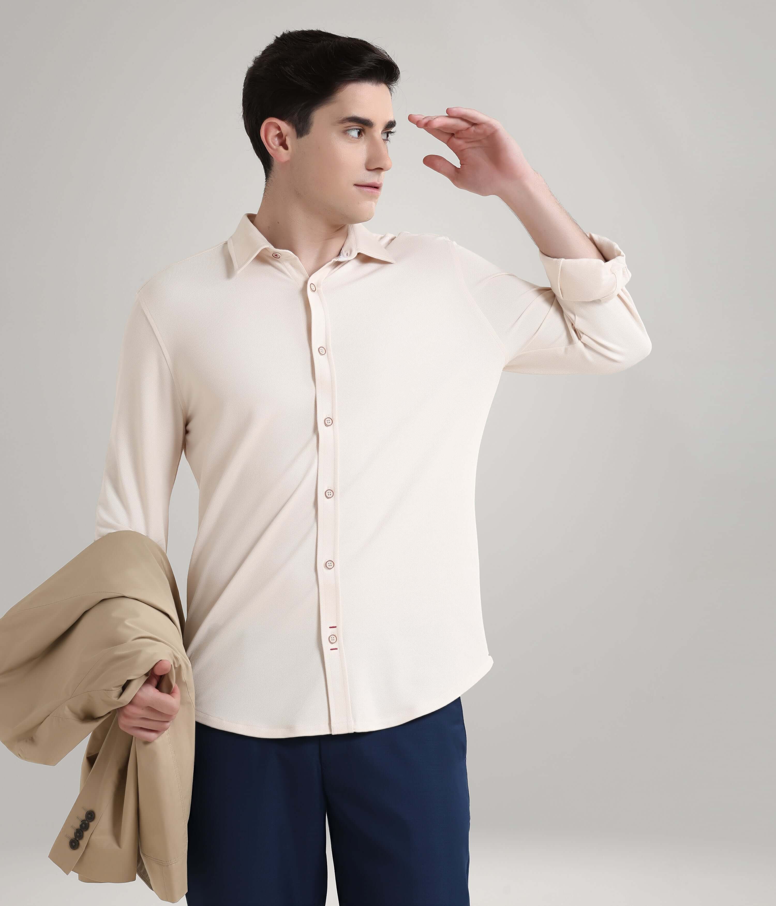 Man wearing dusky beige knitted Turms stretchable shirt, holding a beige jacket, showcasing premium menswear with anti-stain, anti-odor features.