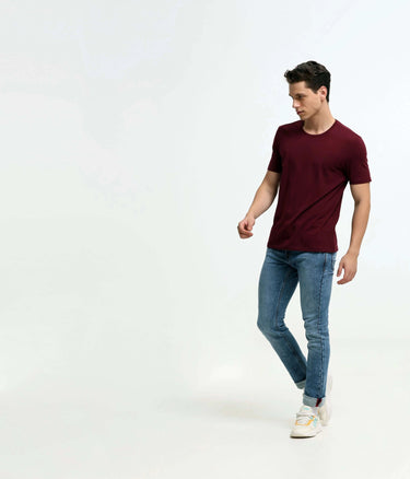Man wearing stain-proof and odor-resistant cranberry round-neck Turms T-shirt, tailored fit, with blue jeans, highlighting men's new menswear.
