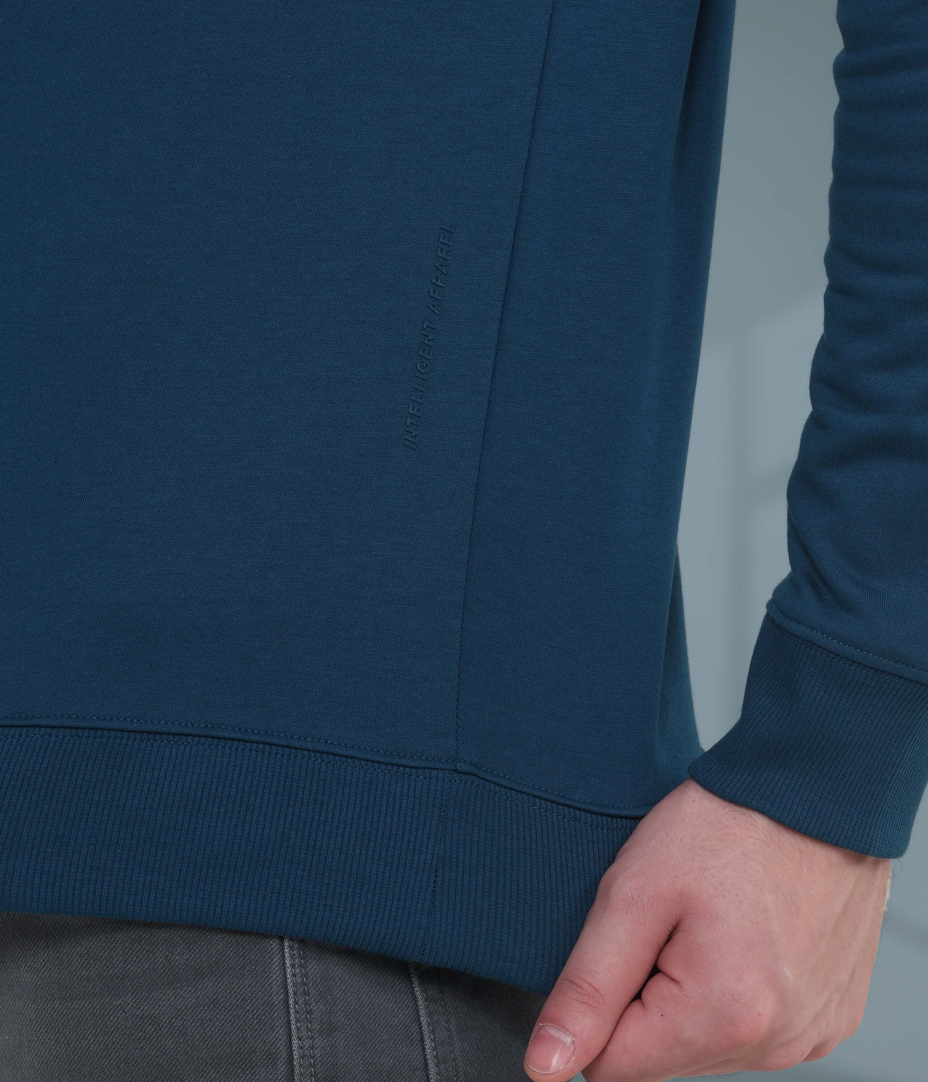 Close-up of a man's hand on the side seam of a blue sweatshirt, showcasing soft, durable cotton-blend fabric.