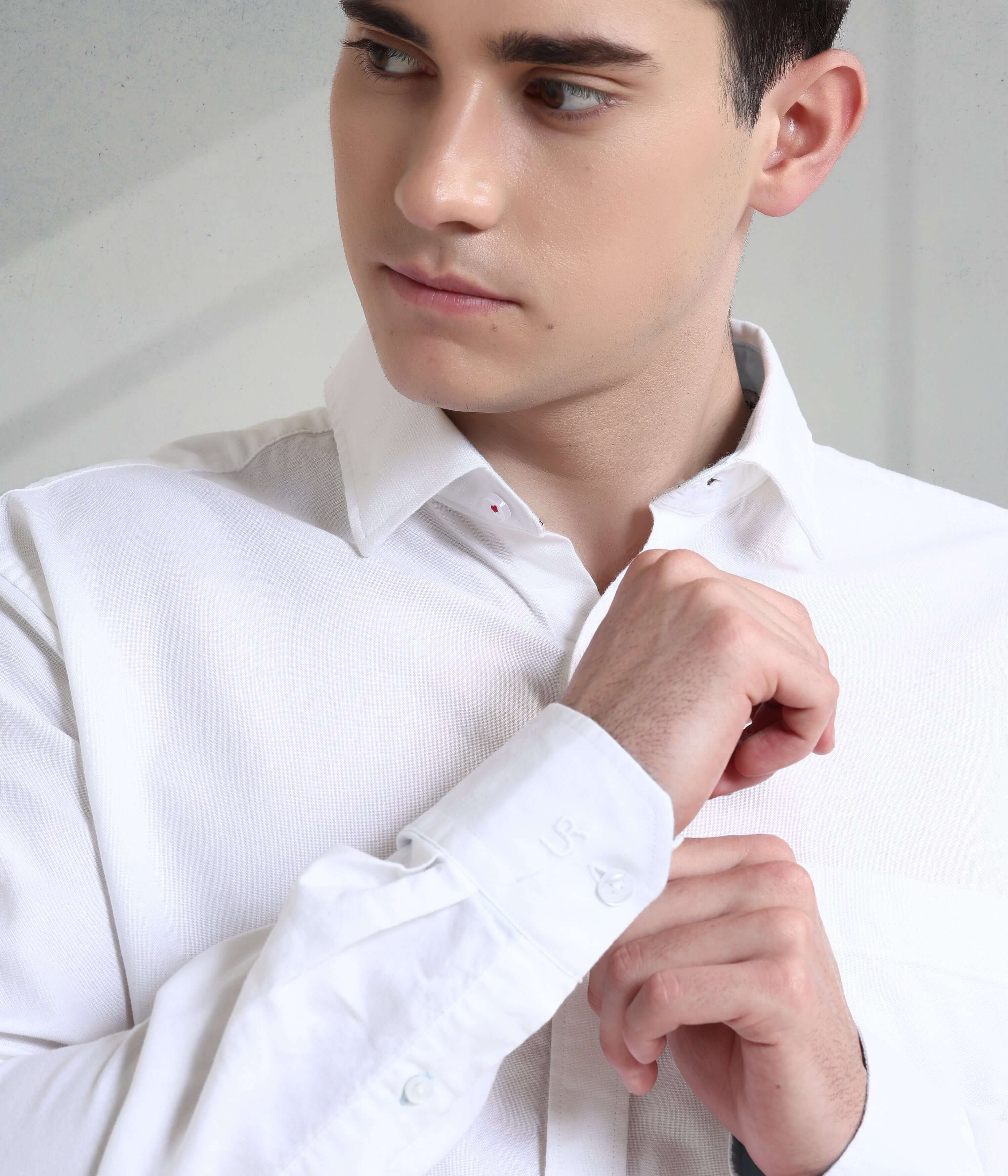 Young man adjusting the cuff of a stylish white Oxford Turms shirt, showcasing its premium quality and elegant design.