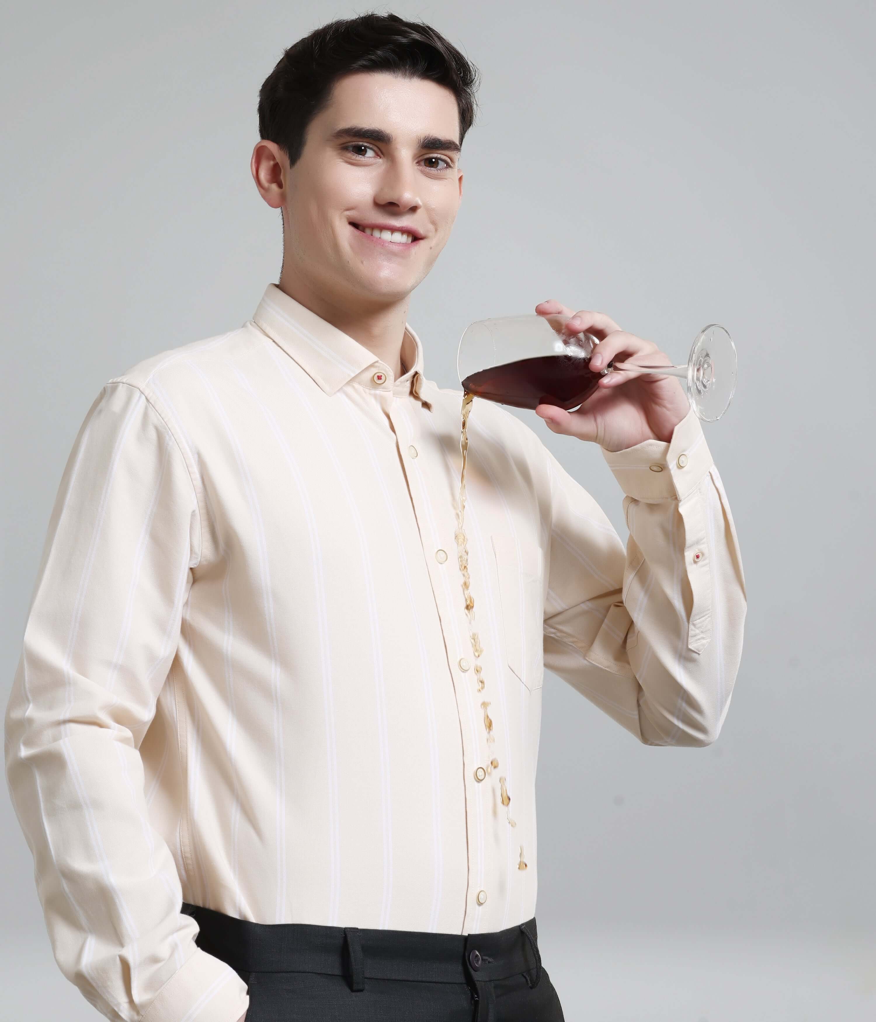 Man in Dessert Beige striped Oxford Turms shirt demonstrating anti-stain feature by pouring wine, showcasing premium menswear.