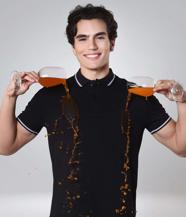 Man wearing a black Turms Polo T-shirt showcasing anti-stain feature with liquid spilling without leaving marks