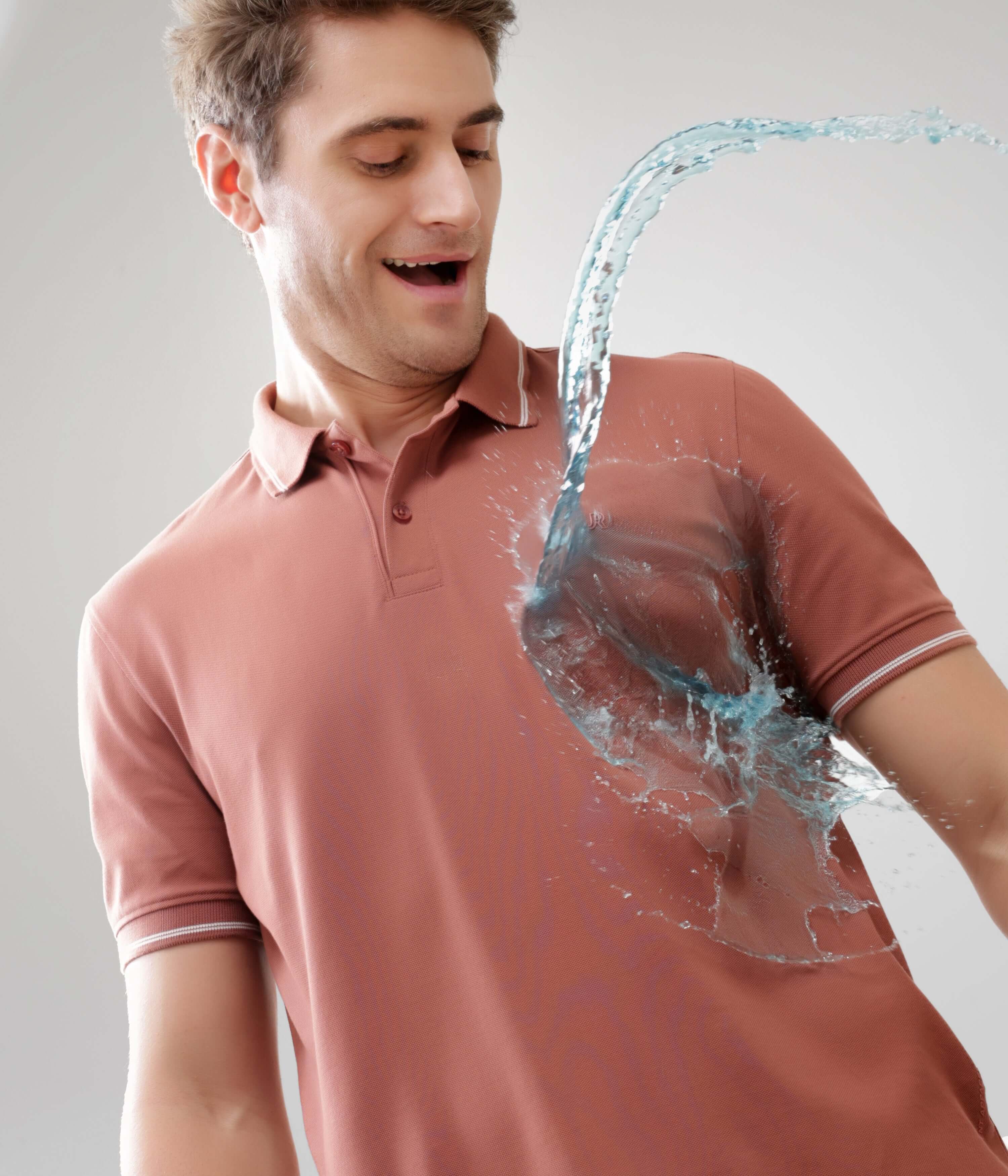 Man in Luxe Cocoa Turms Polo T shirt demonstrating anti-stain, water-resistant feature with water splash, made of premium cotton and spandex.