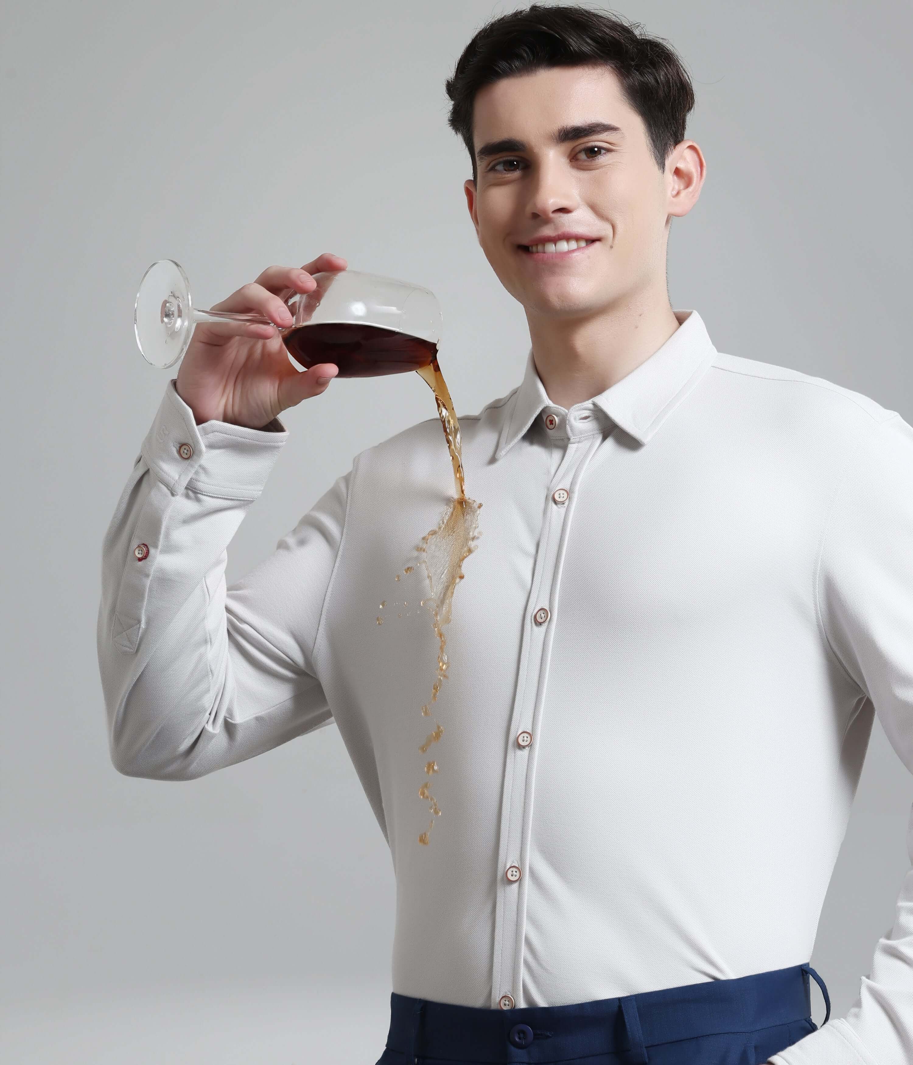 Man wearing Ashen Grey Knitted Turms Stretchable Shirt, demonstrating anti-stain feature with a drink spill.