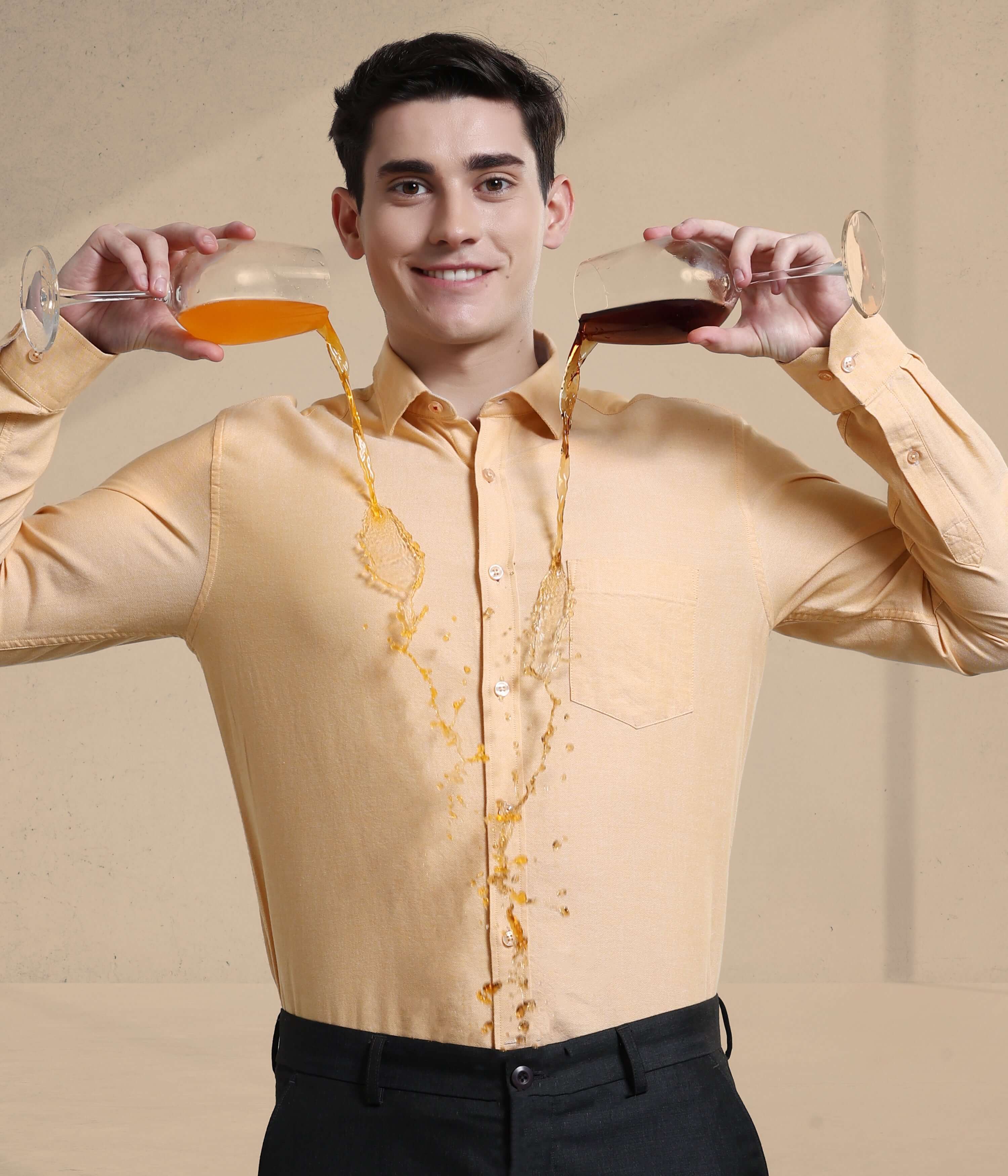 Man in sandy-colored Oxford shirt demonstrating anti-stain features by pouring drinks without worry.