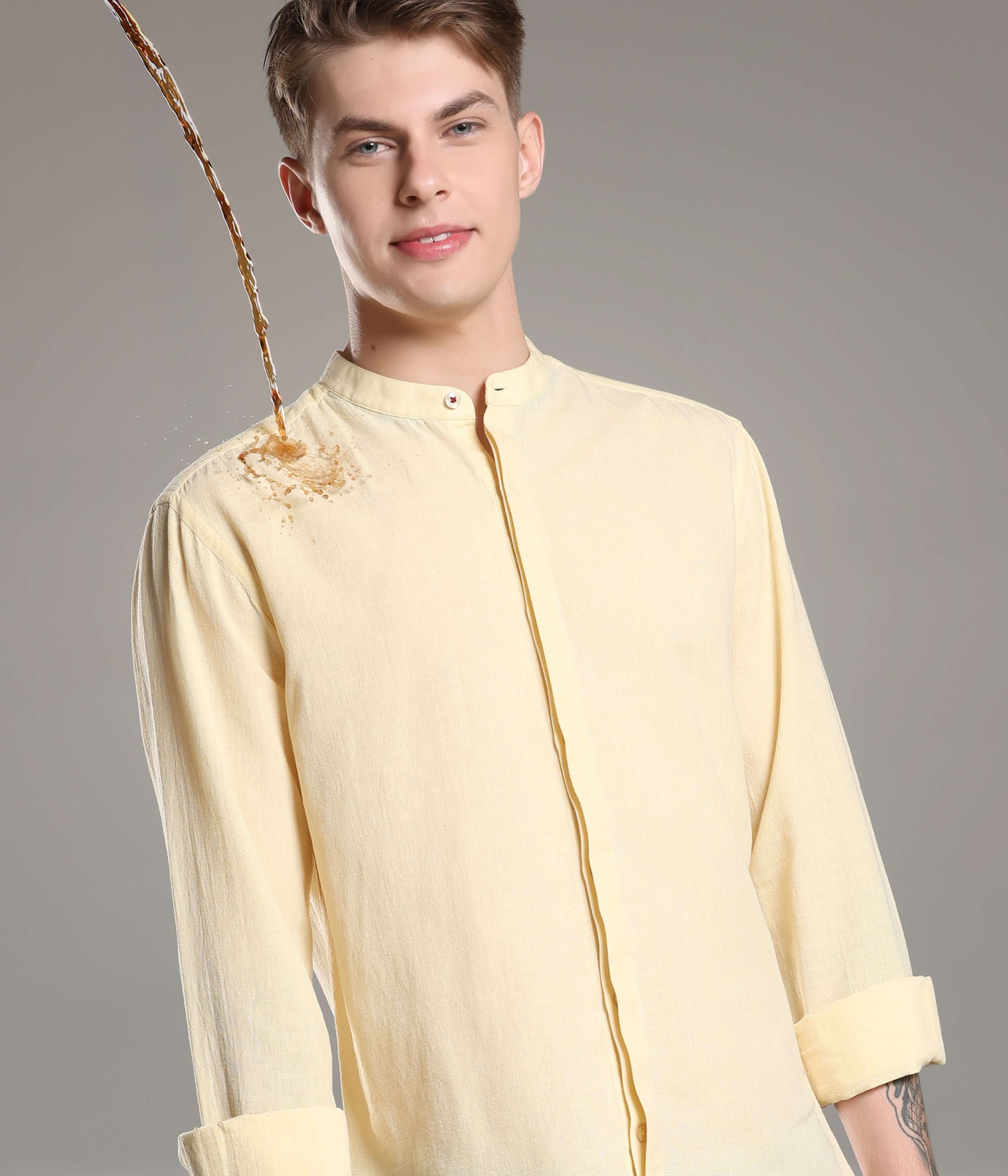 A man wearing a pastel yellow Cotton/Linen Turms shirt with a mandarin collar demonstrating the shirt’s antistain capability as liquid spills on it.