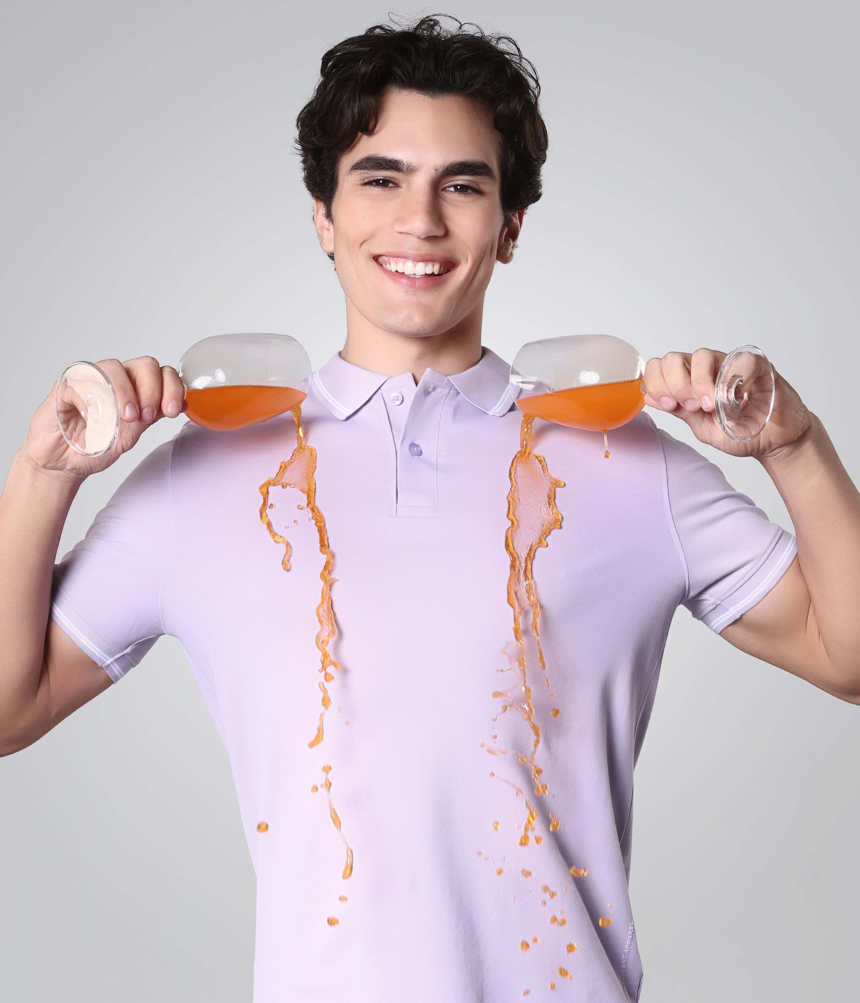 Man wearing a stain-resistant Turms Polo T-shirt in light purple, demonstrating anti-stain technology with drinks spilling but not staining.