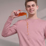 Young man in a pink sweatshirt demonstrating its stain-proof features by pouring juice, showcasing style and functionality.