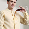 Man wearing pastel yellow linen shirt with mandarin collar and demonstrating anti-stain feature by pouring liquid on it.