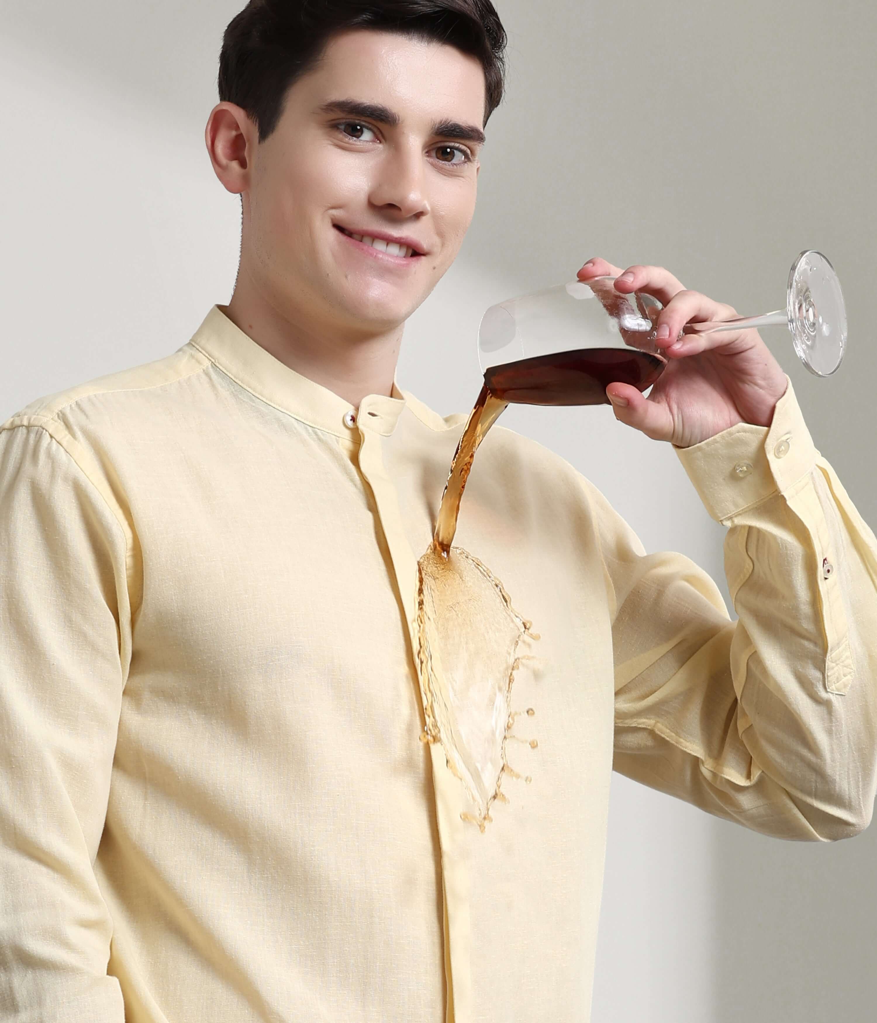 Man wearing pastel yellow linen shirt with mandarin collar and demonstrating anti-stain feature by pouring liquid on it.