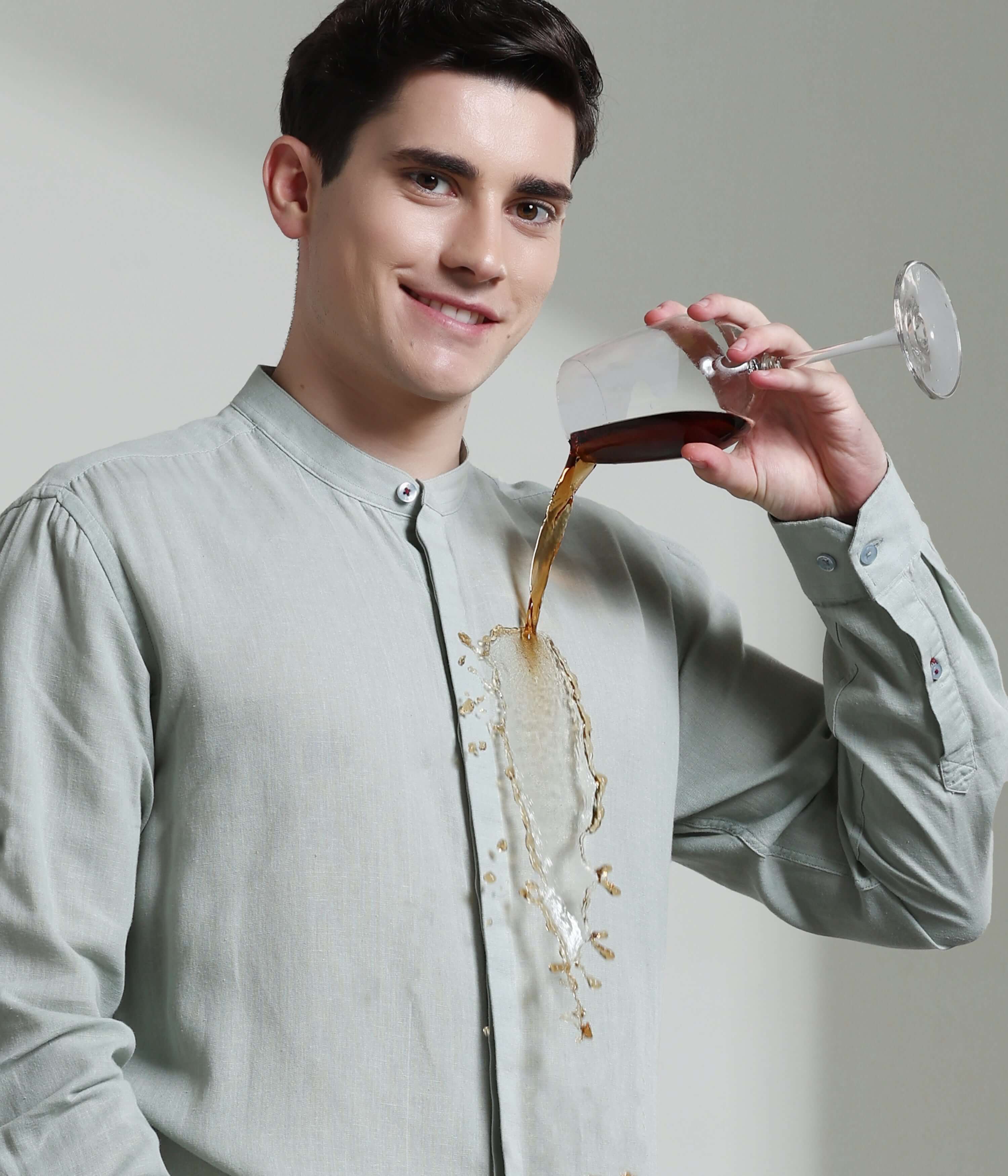 Man wearing storm grey linen shirt with mandarin collar demonstrates anti-stain feature as drink spills without leaving a mark.