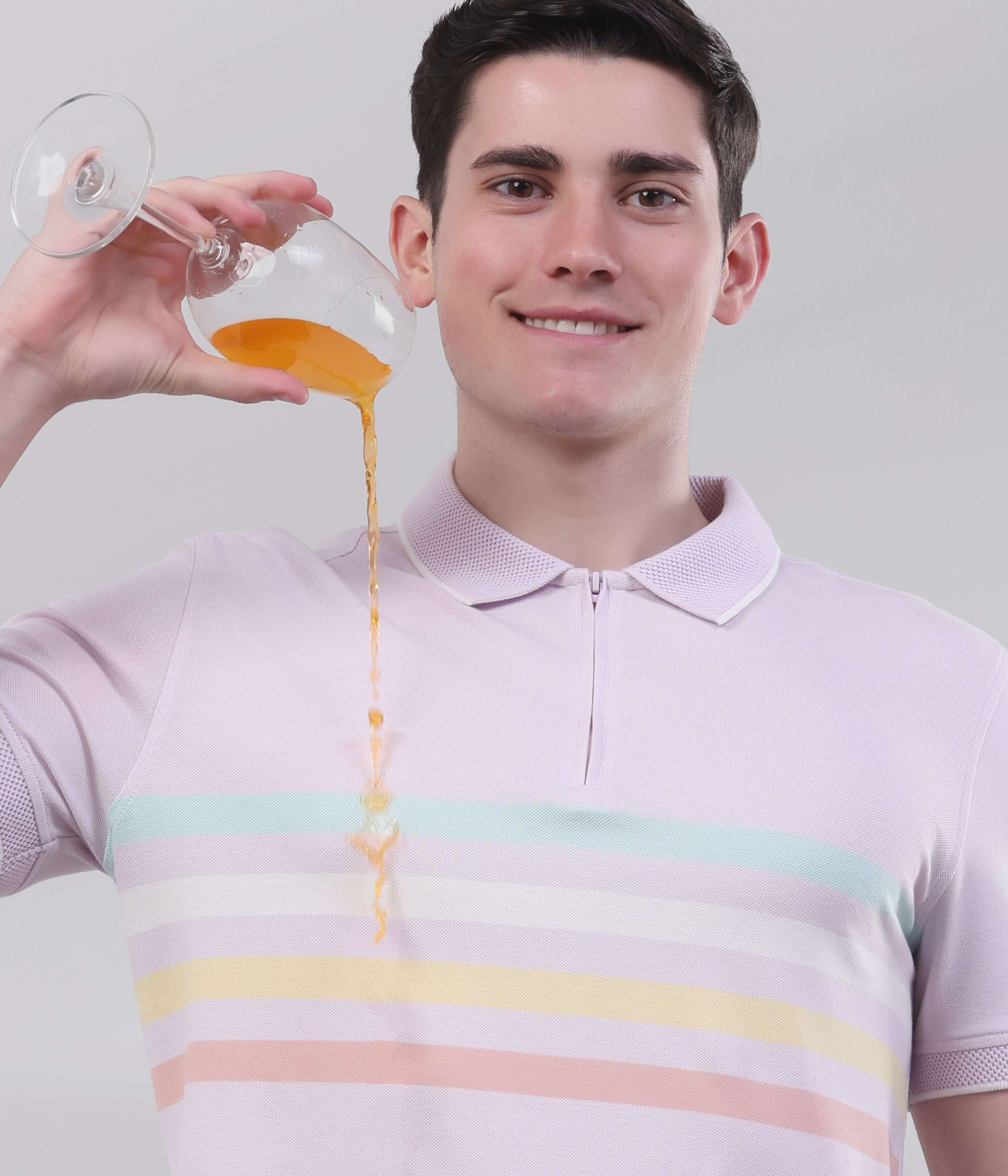 Man in lavender polo shirt demonstrating the anti-stain feature by pouring juice without worry.