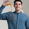 Man wearing Onyx Teal Turms shirt with mandarin collar, demonstrating anti-stain feature by pouring liquid on linen fabric.