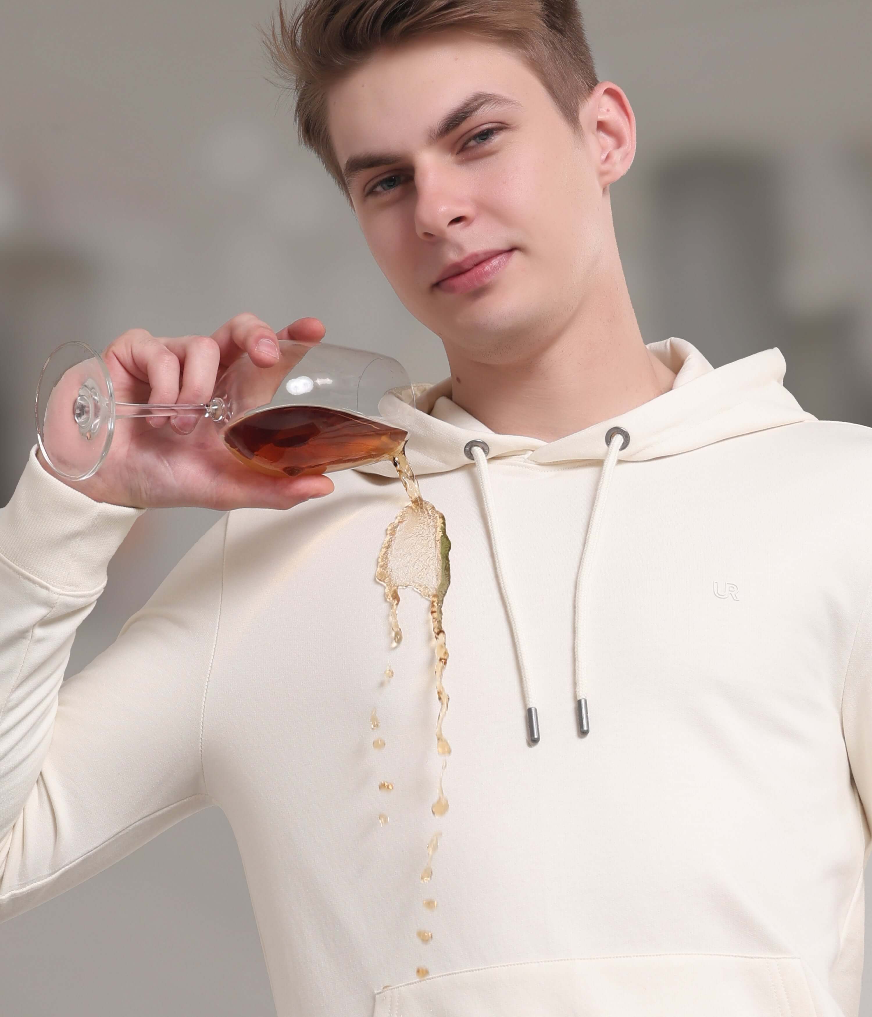 Man in cream waterproof hoodie pouring drink, showcasing stain-proof and stylish design for everyday wear.