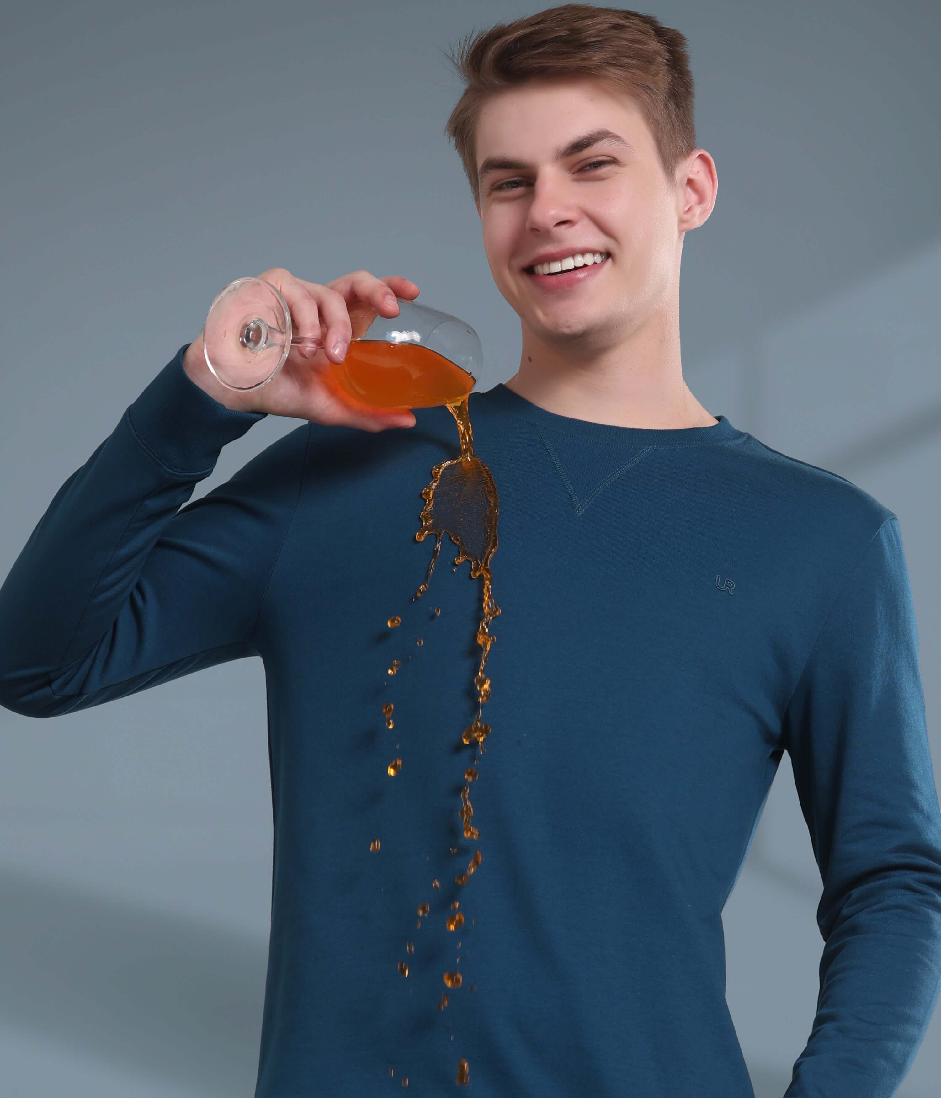 Model wearing a blue sweatshirt, showcasing its waterproof and stain-proof features while pouring a beverage.