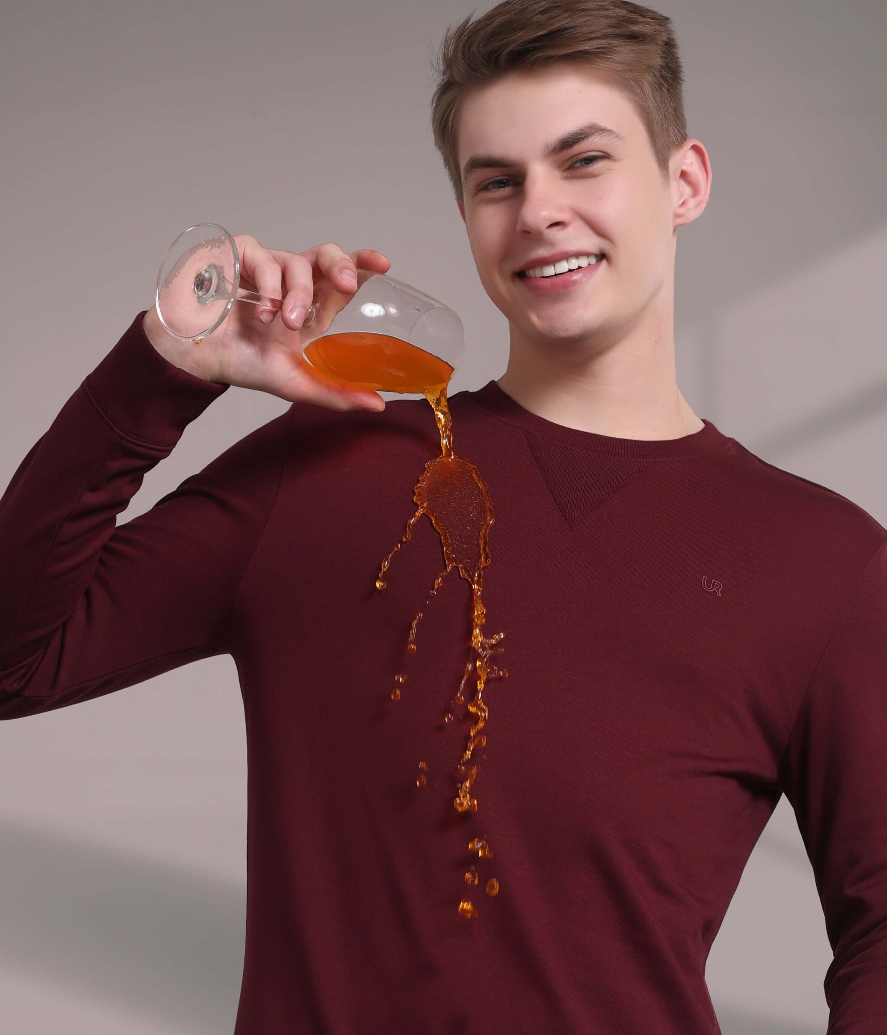 Man in maroon sweatshirt demonstrating waterproof feature while pouring drink without stains, showcasing anti-odor technology.