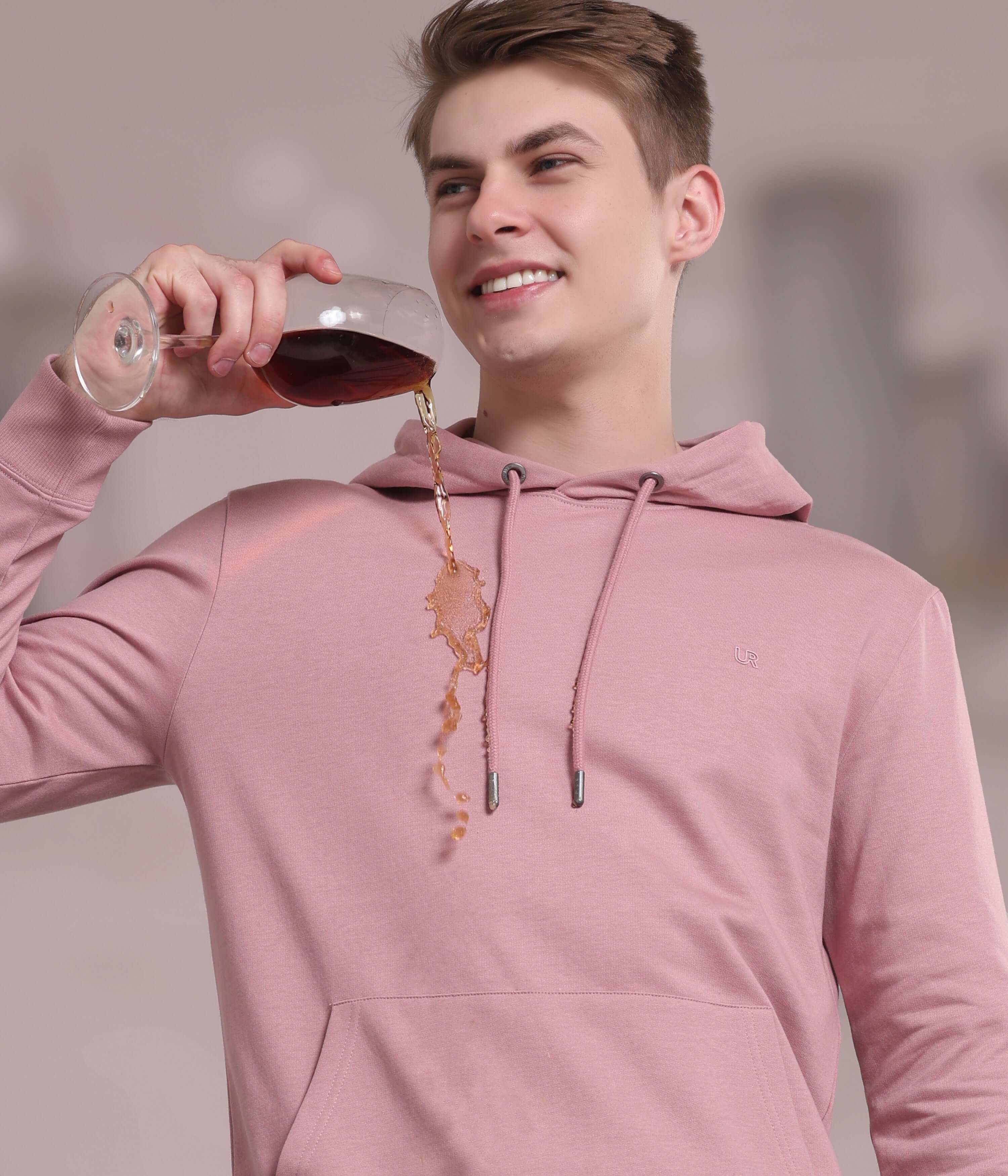 Stylish man in pink musing hoodie showcasing waterproof, stain-proof functionality while enjoying a drink.