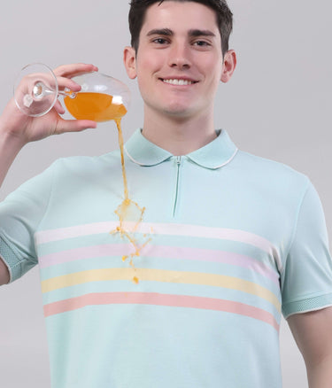 Man wearing a blue origami polo shirt, demonstrating its anti-stain feature with a drink, highlighting its stylish design.