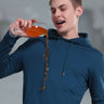 Young man wearing a blue hooded sweatshirt, demonstrating its waterproof and stain-proof features while pouring a drink.