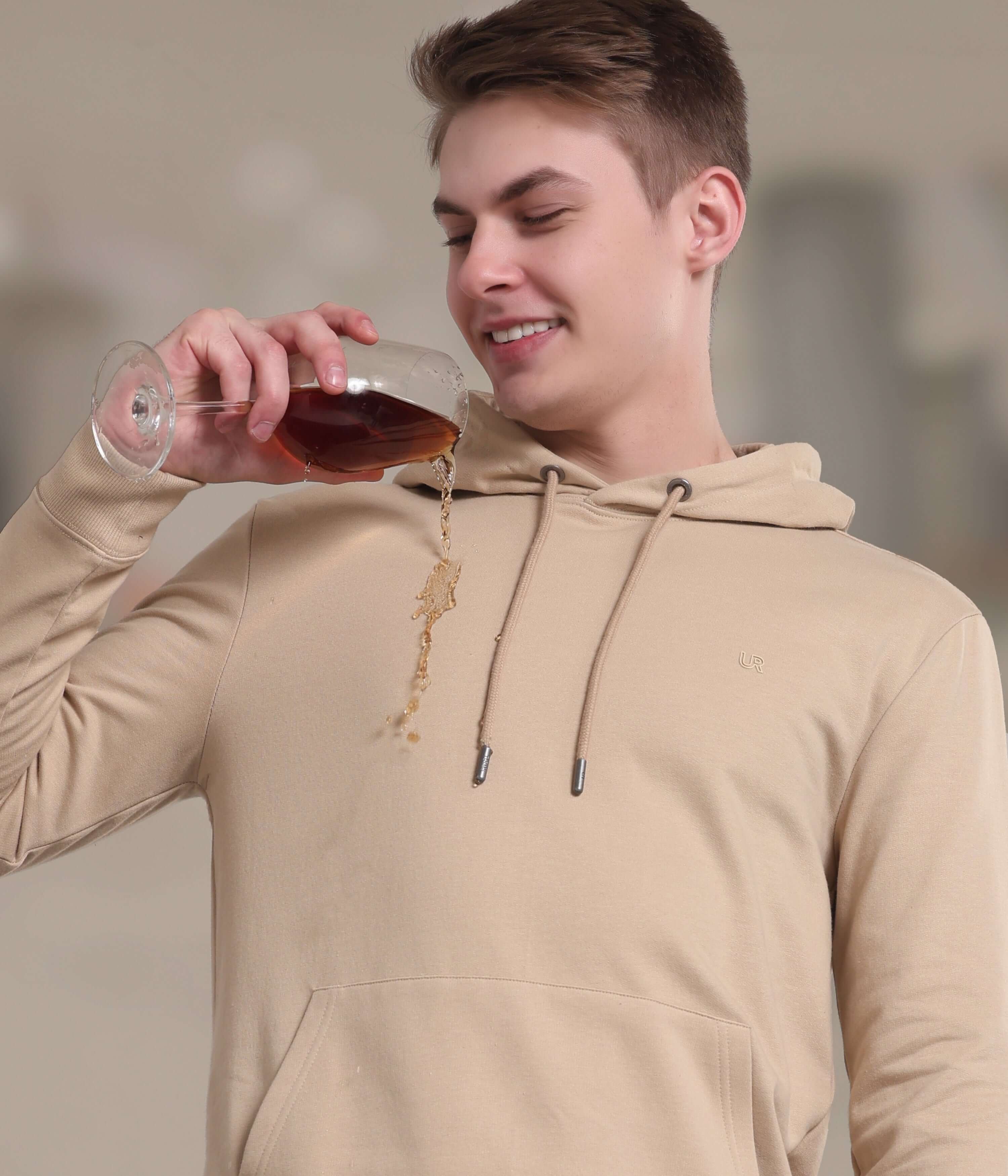 Man in a camel-colored hooded sweatshirt enjoying a drink, showcasing stain-proof and durable fabric features.