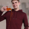 Model in a burgundy hooded sweatshirt demonstrating its waterproof, stain-proof features by spilling a drink.