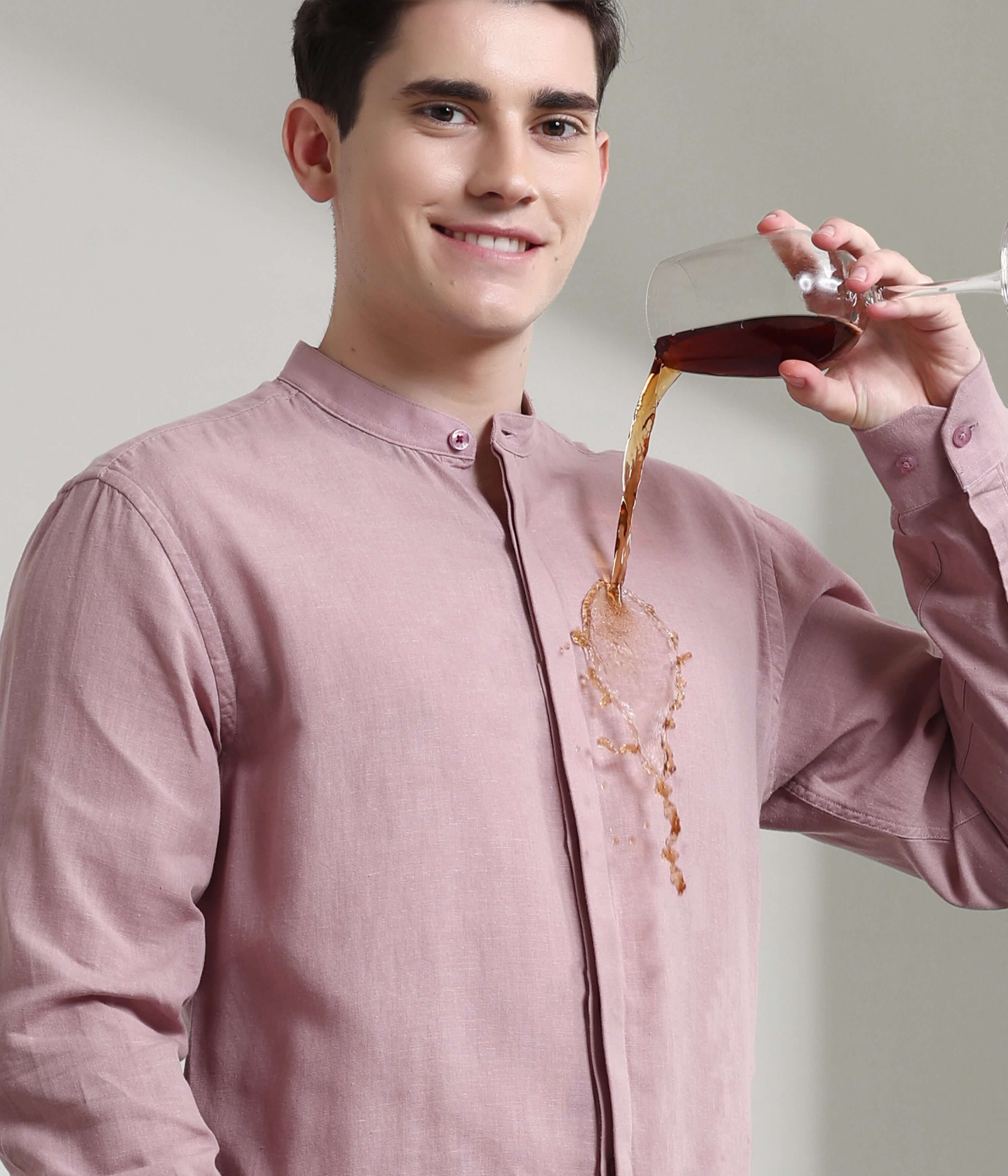 Man wearing a Wood Rose Turms linen shirt with mandarin collar, demonstrating anti-stain feature by pouring a drink on it.