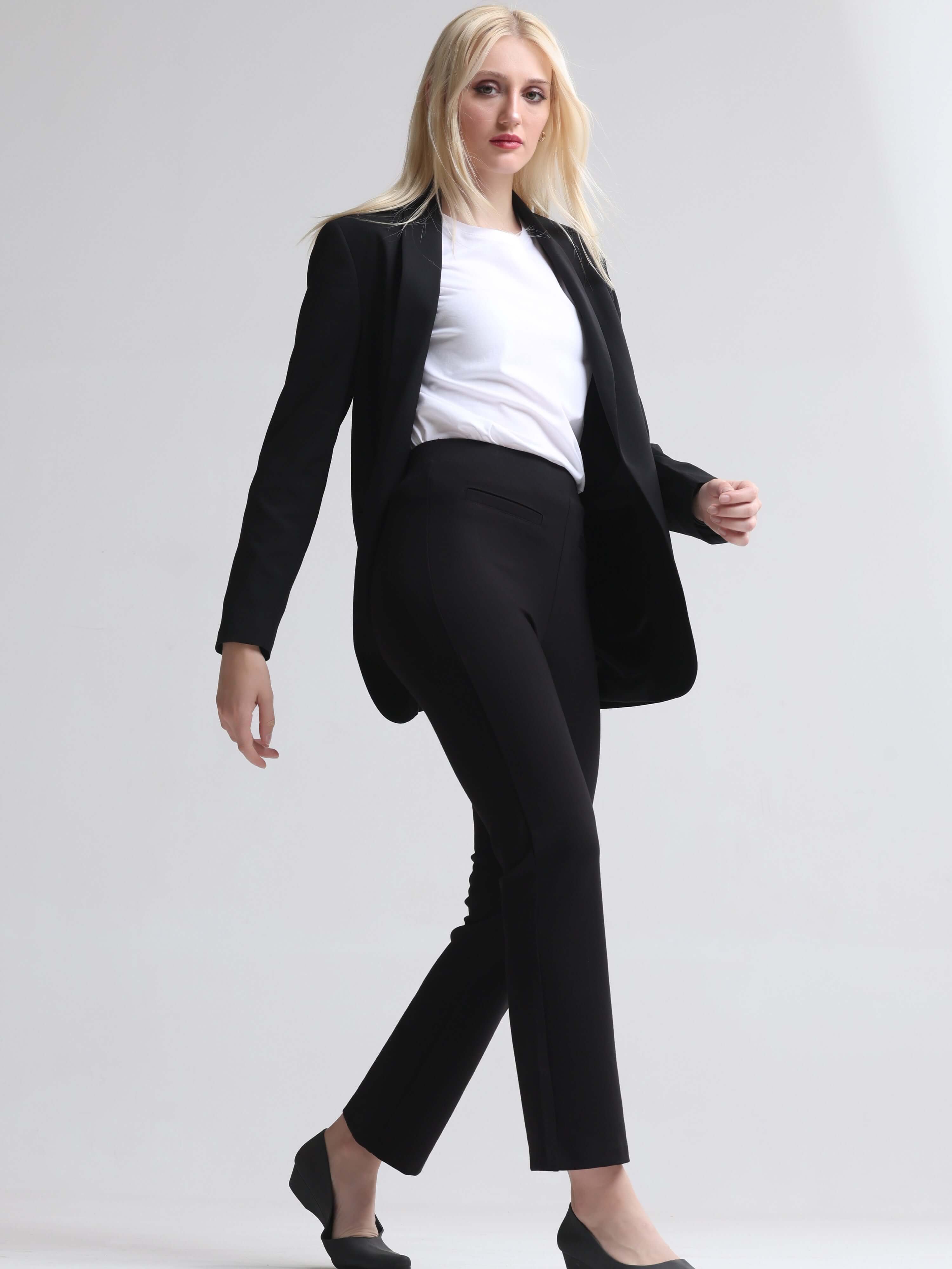 Woman wearing a white round-neck T-shirt, black blazer, and black pants in a stylish, professional look while walking.