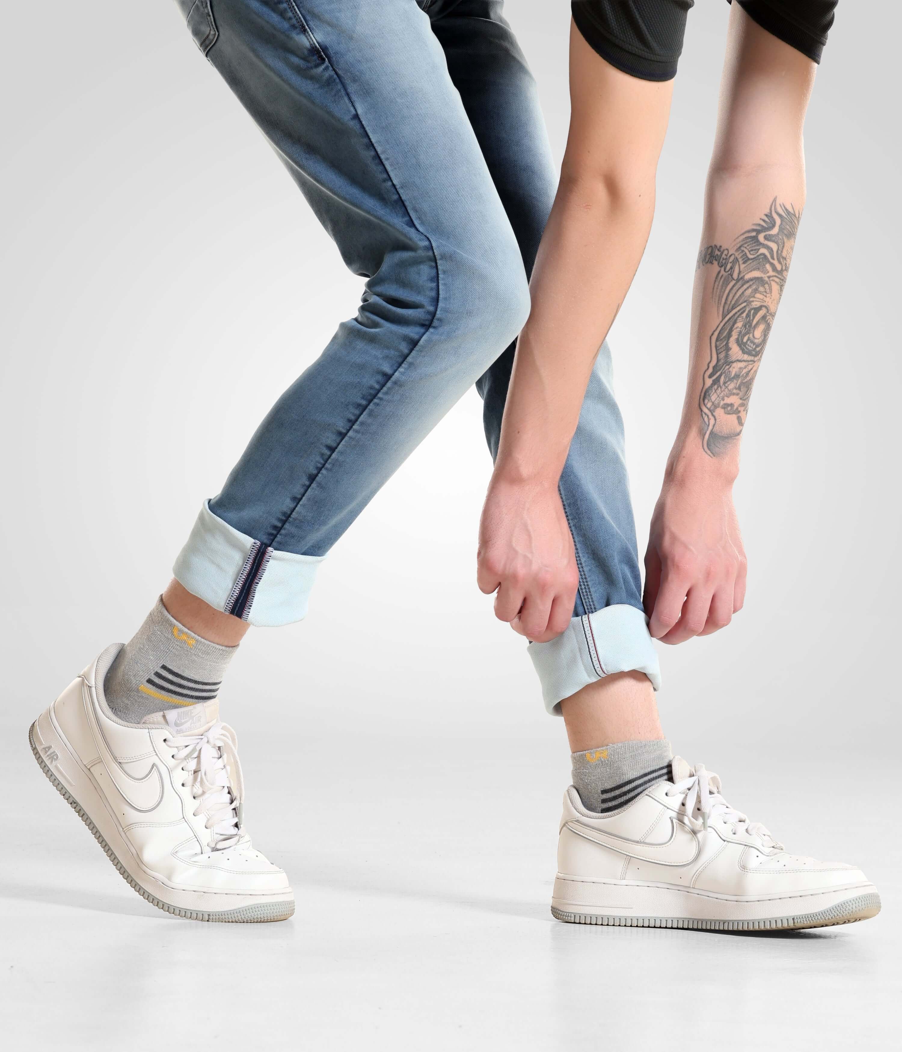 Man wearing Blue Birdy high-performance denim pants from Turms Intelligent Apparel, cuffing the jeans and showcasing white sneakers.