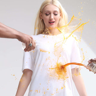 Woman wearing a white stain-proof and odor-resistant Turms T-shirt, demonstrating its spill-repellent quality with liquid being poured.