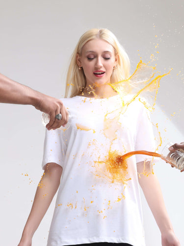 Woman wearing a white stain-proof and odor-resistant Turms T-shirt, demonstrating its spill-repellent quality with liquid being poured.