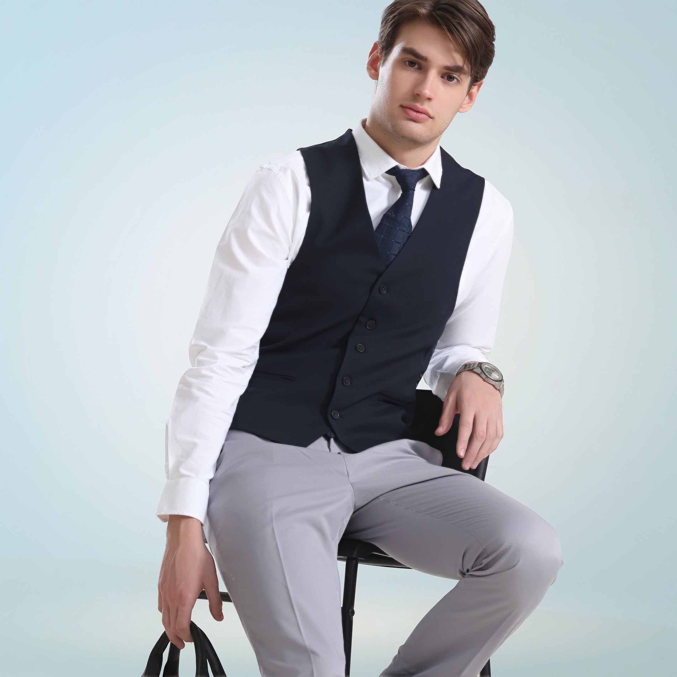 Man in a white Oxford Turms shirt and black vest seated against a light blue background