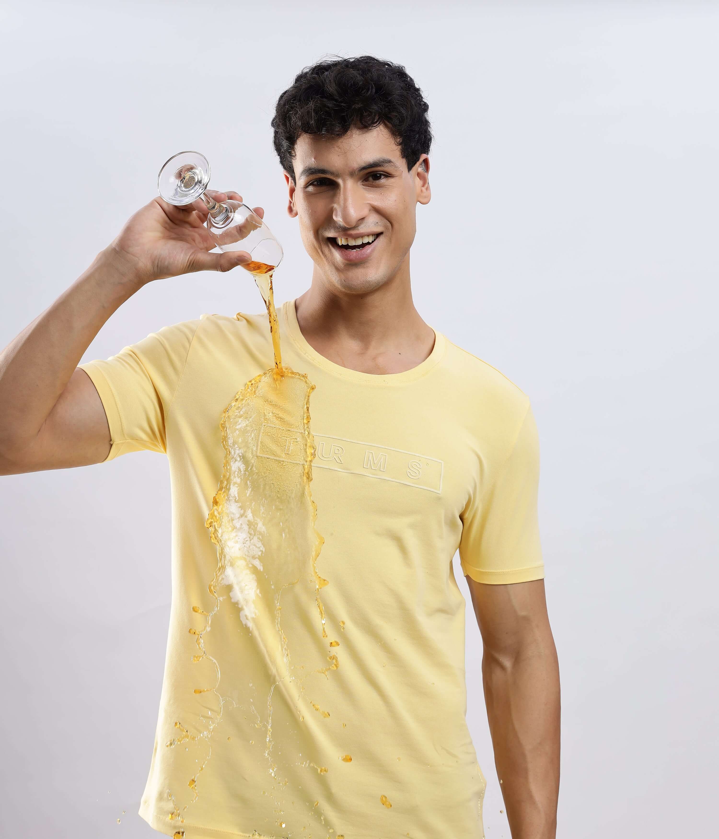 Aura Yellow cotton t-shirt, stretchable and waterproof, showcased by a smiling man spilling liquid from a glass.